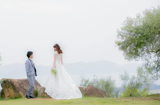 海の見える広場でウェディングドレスを着た新婦とタキシードを着た新郎が向き合って経っているウェディングフォトもスタジオグッドにお任せ