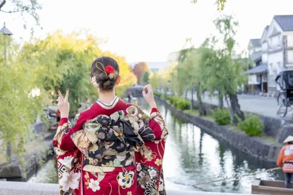 川沿いで振袖の帯とアップスタイルの髪型を見せる女性の後ろ姿の写真