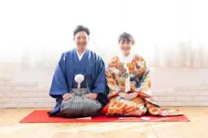 岡山のスタジオで青の紋付袴と色打掛を着た新郎新婦様が並んで座るフォトウェディングの一枚