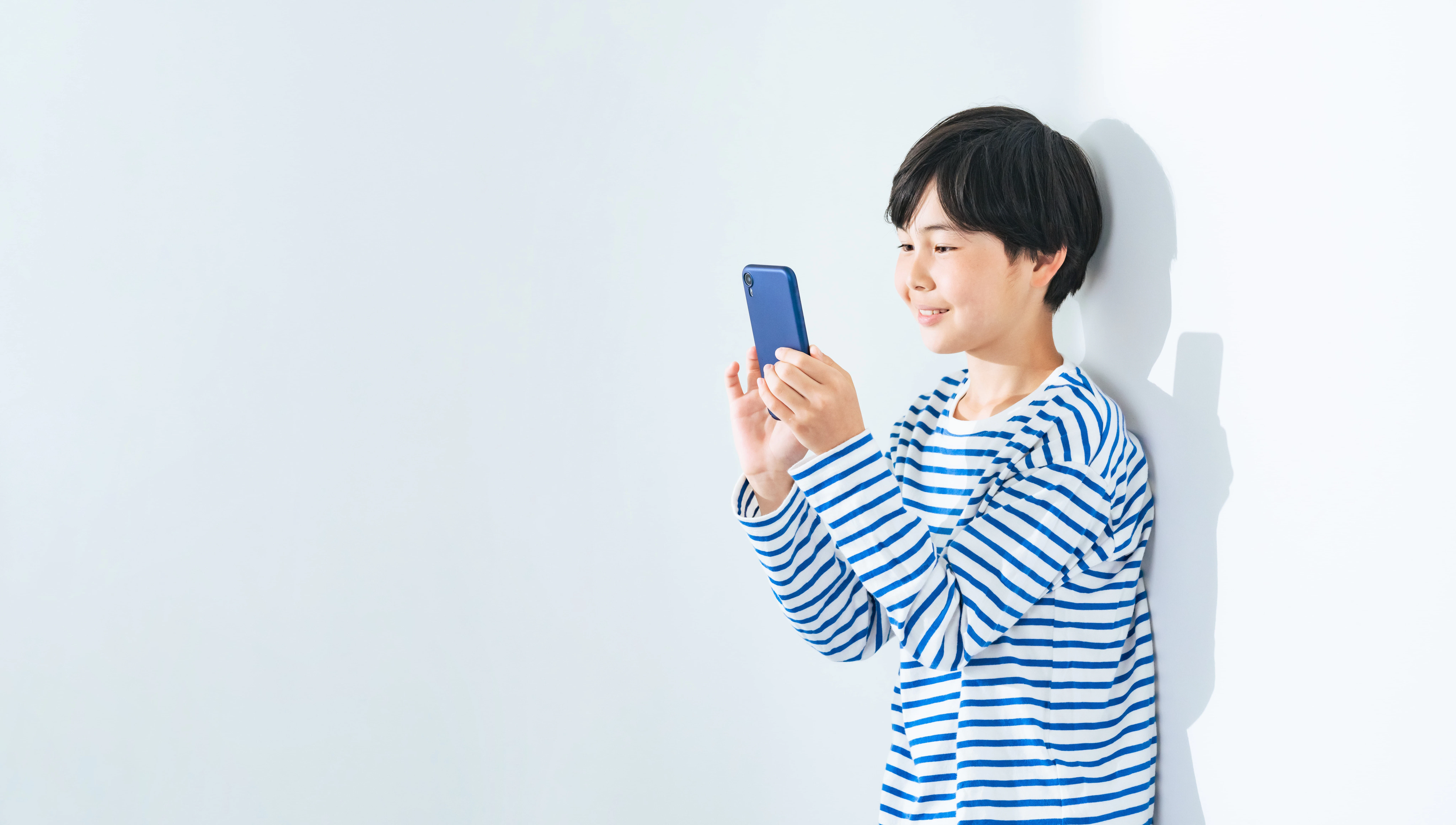 壁にもたれてスマホを見つめる少年