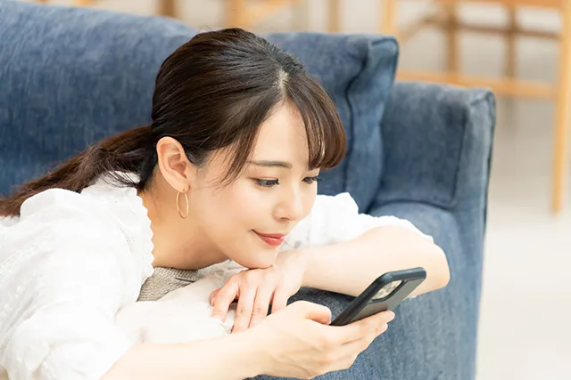 ソファに横になりながらスマホをいじる女性