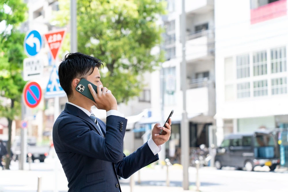 通話をしながら2台目のスマホを見るビジネスパーソン