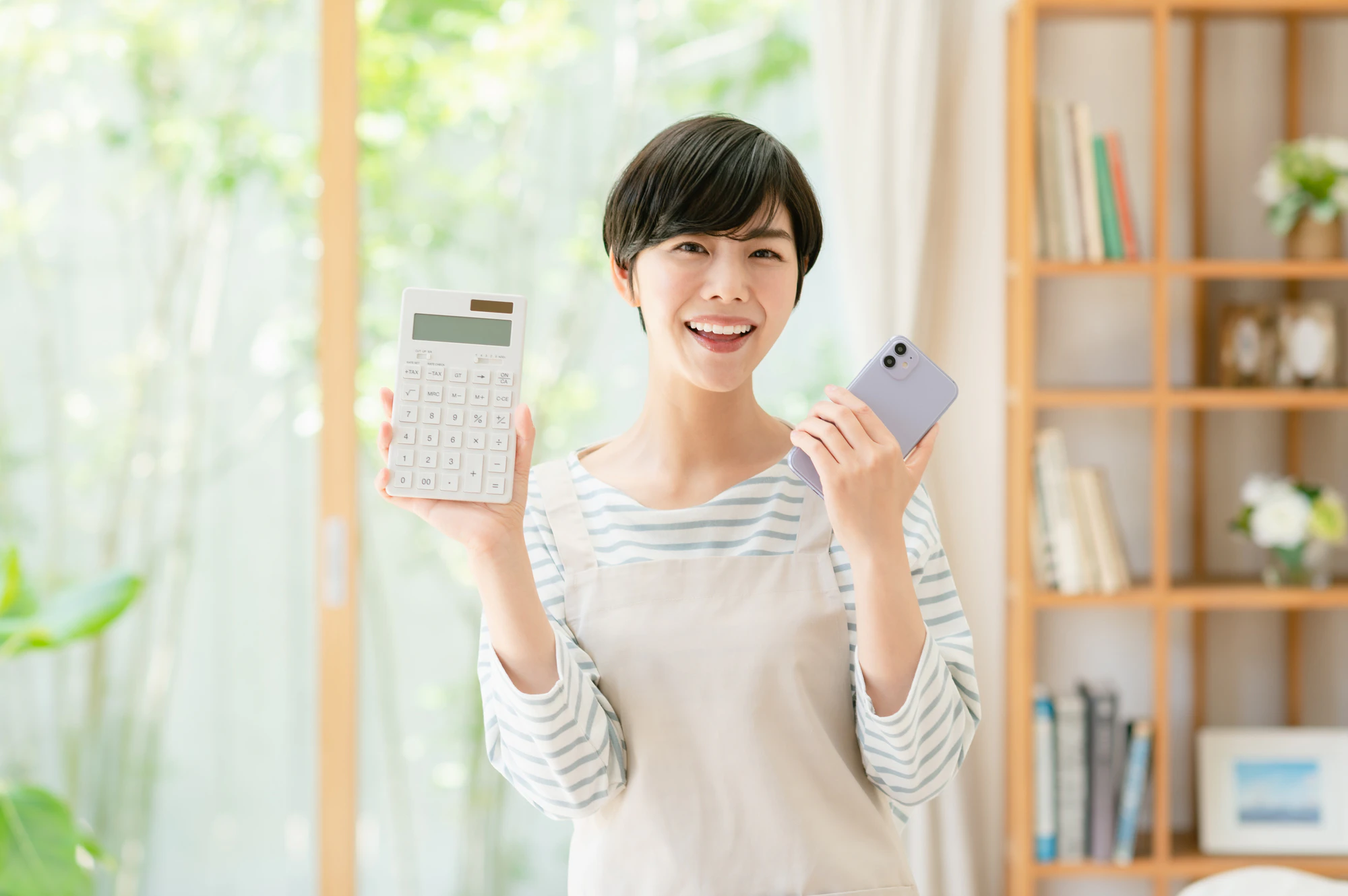 スマホと電卓を持つ若い女性