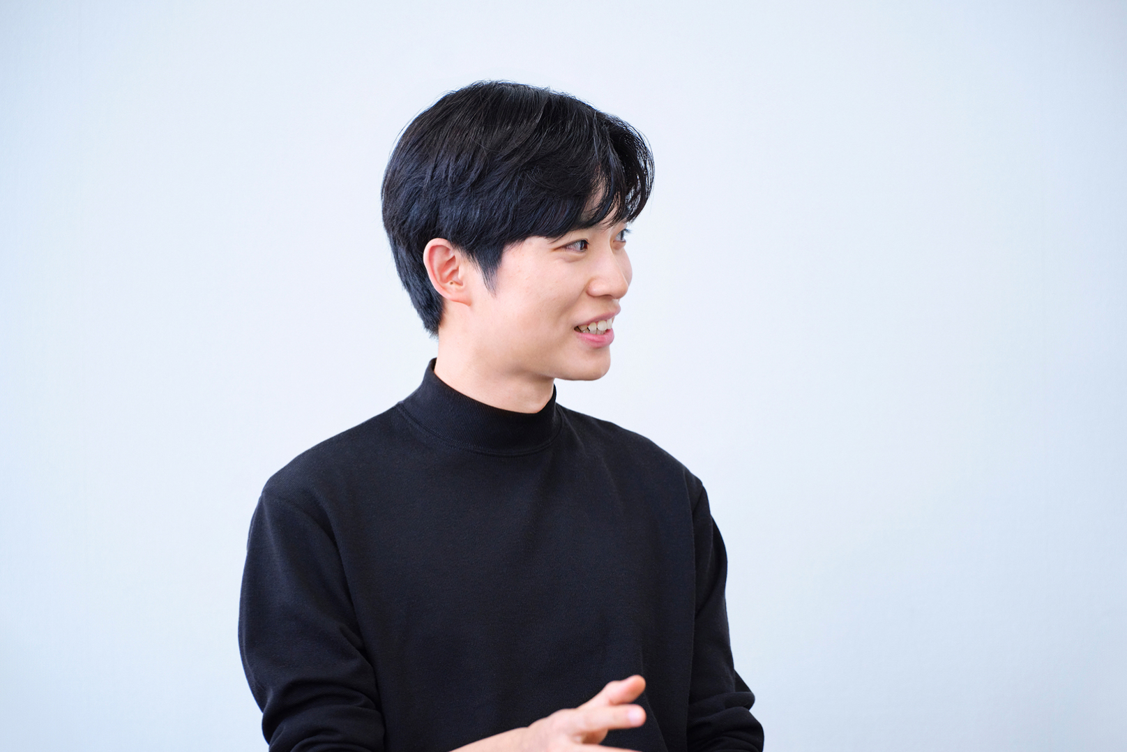 黒いハイネックを着た短髪の男性が微笑みながら横を向いている様子。