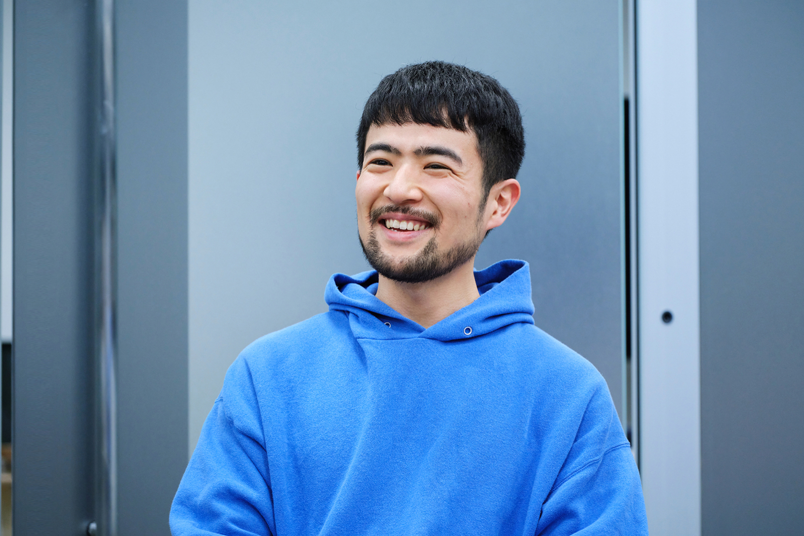 青いパーカーを着た笑顔の若い男性の上半身写真。