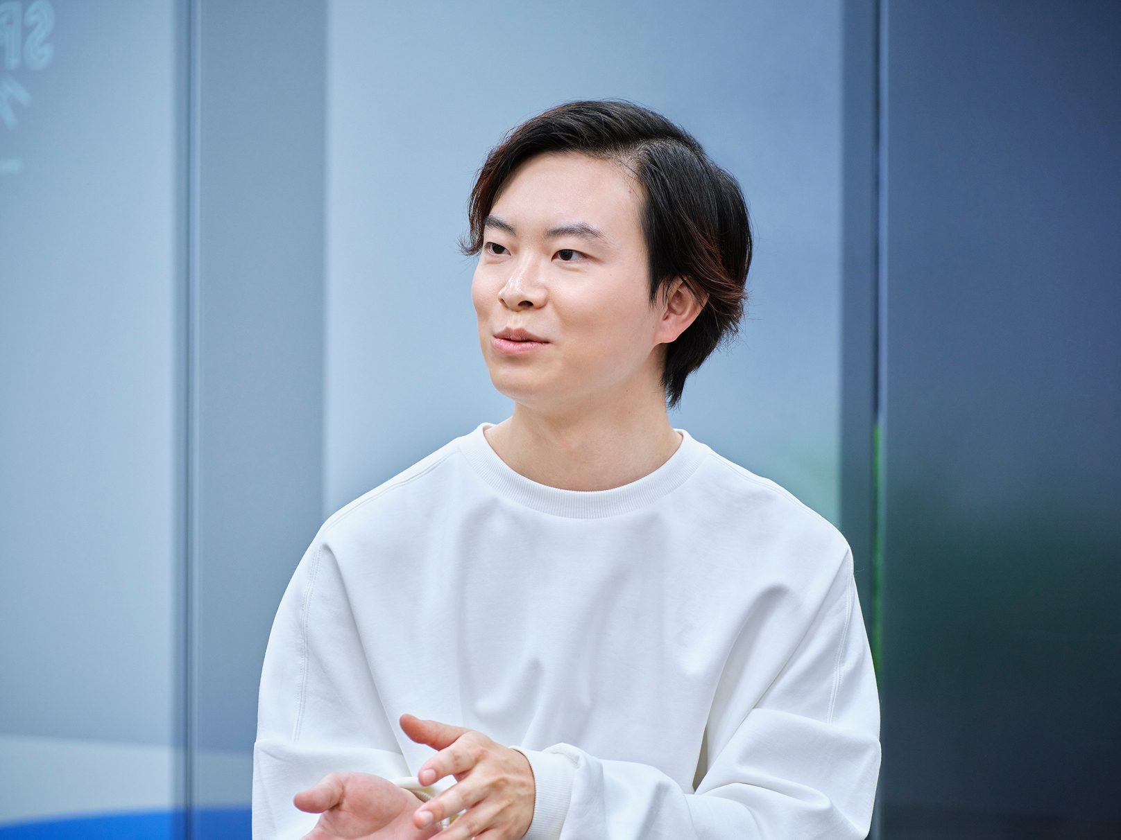 若い男性が白いシャツを着て、やや横を向いて立っている。表情は穏やかで思慮深そう。