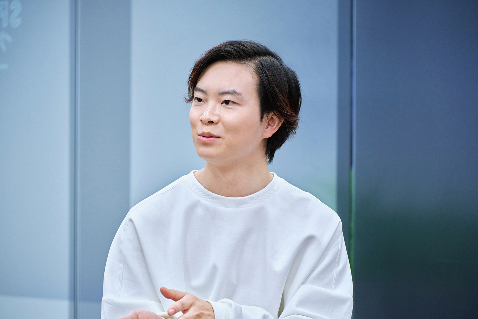 若い男性が白いシャツを着て、やや横を向いて立っている。表情は穏やかで思慮深そう。