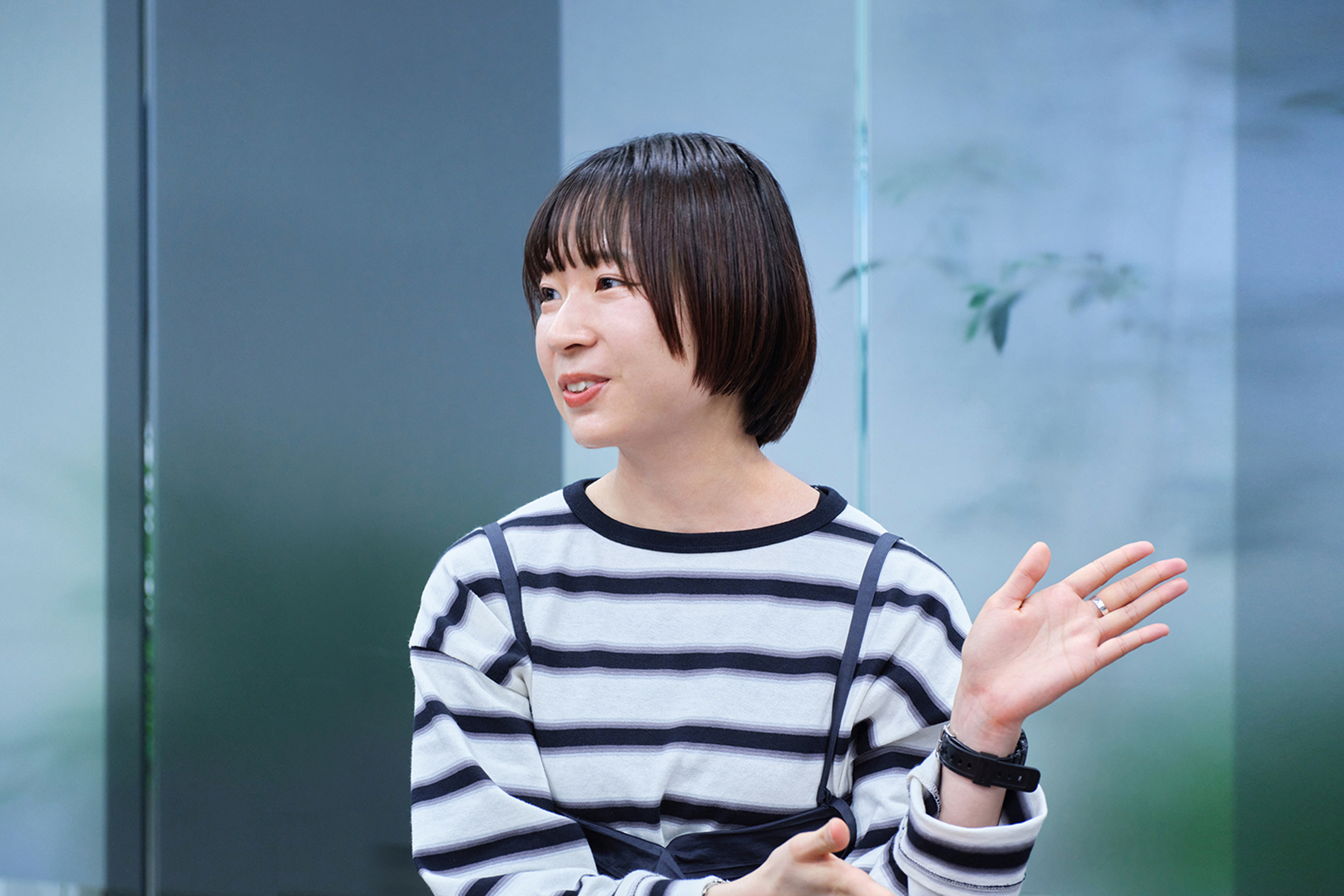 縞模様のトップスを着たボブヘアーの女性が笑顔で手を上げている写真