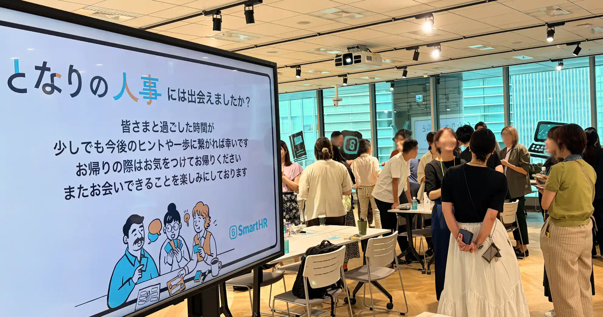 「となりの人事には出会えましたか?」と表示されたモニターと、会場内で立ち話をする人々の様子