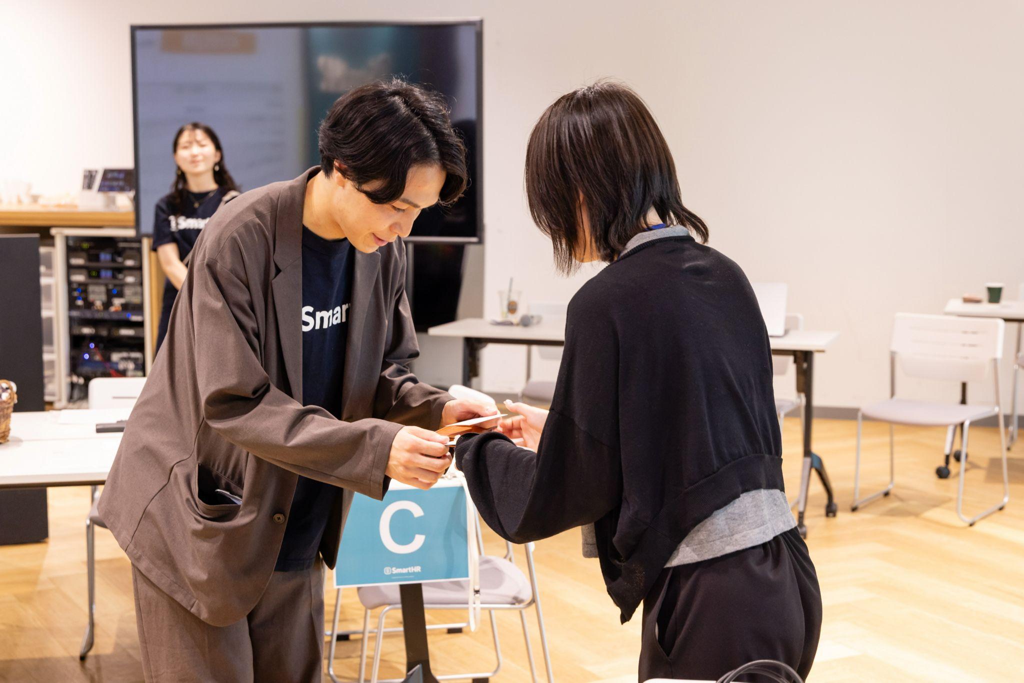 イベント会場で名刺交換をする2人。左側の男性はSmartHRのロゴ入りTシャツにジャケットを羽織っている
