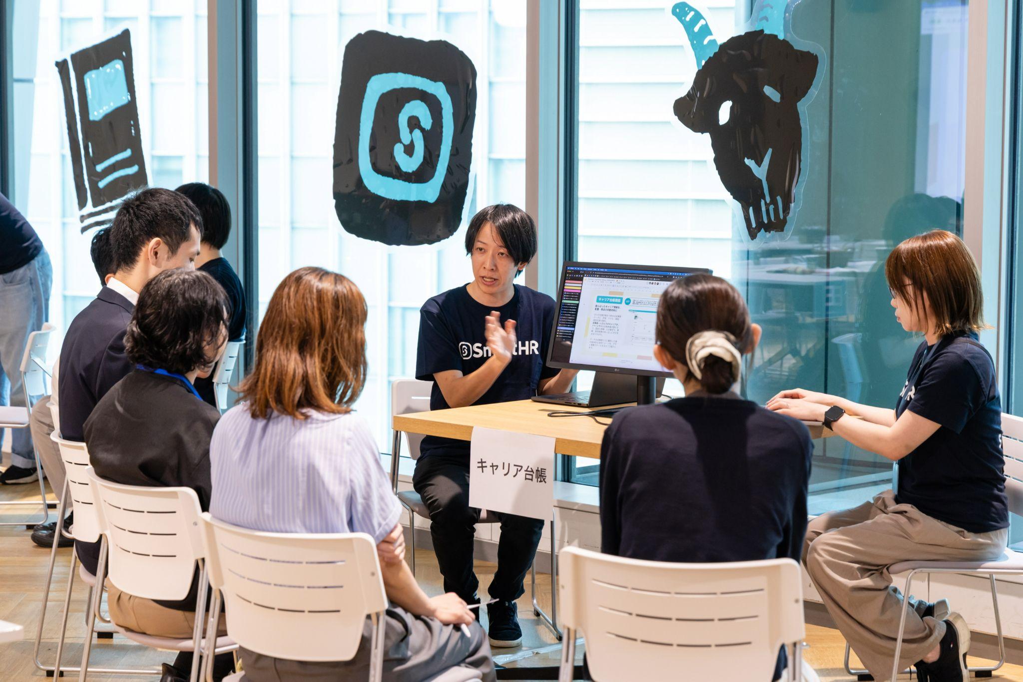 「キャリア台帳」の卓札があるテーブルで、モニターを使って参加者に説明をしているSmartHRのTシャツを着た男性