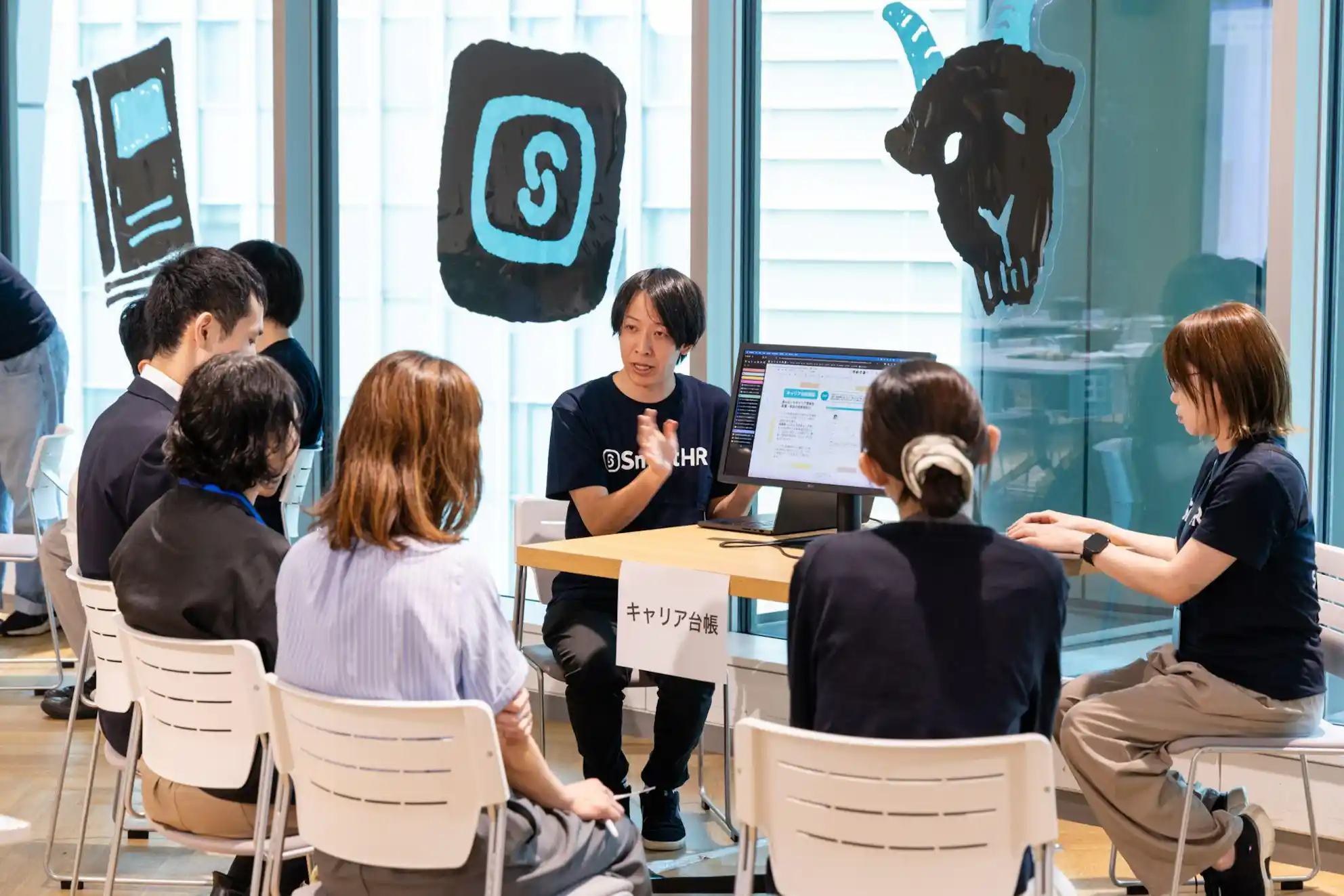 「キャリア台帳」の卓札があるテーブルで、モニターを使って参加者に説明をしているSmartHRのTシャツを着た男性