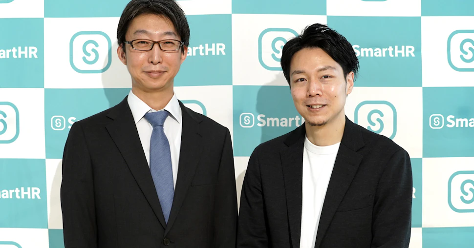 SmartHRロゴが入ったバックパネルを背景に、代表取締役CEO芹澤と取締役COO倉橋が横並びで映ったバストアップ写真