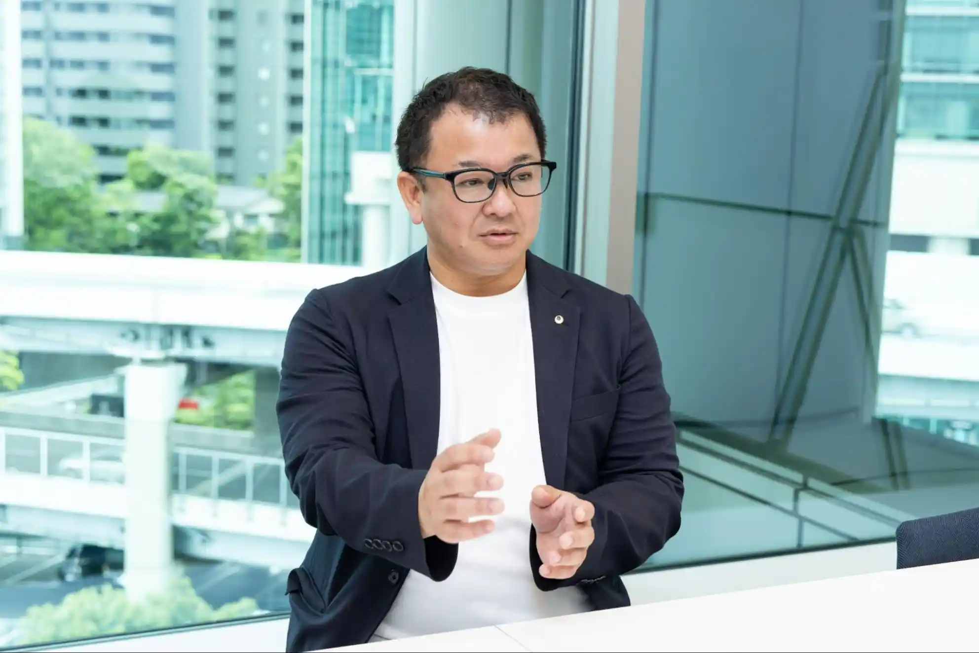 オフィスの窓際で、身振り手振りを交えてインタビューに答える田川さん