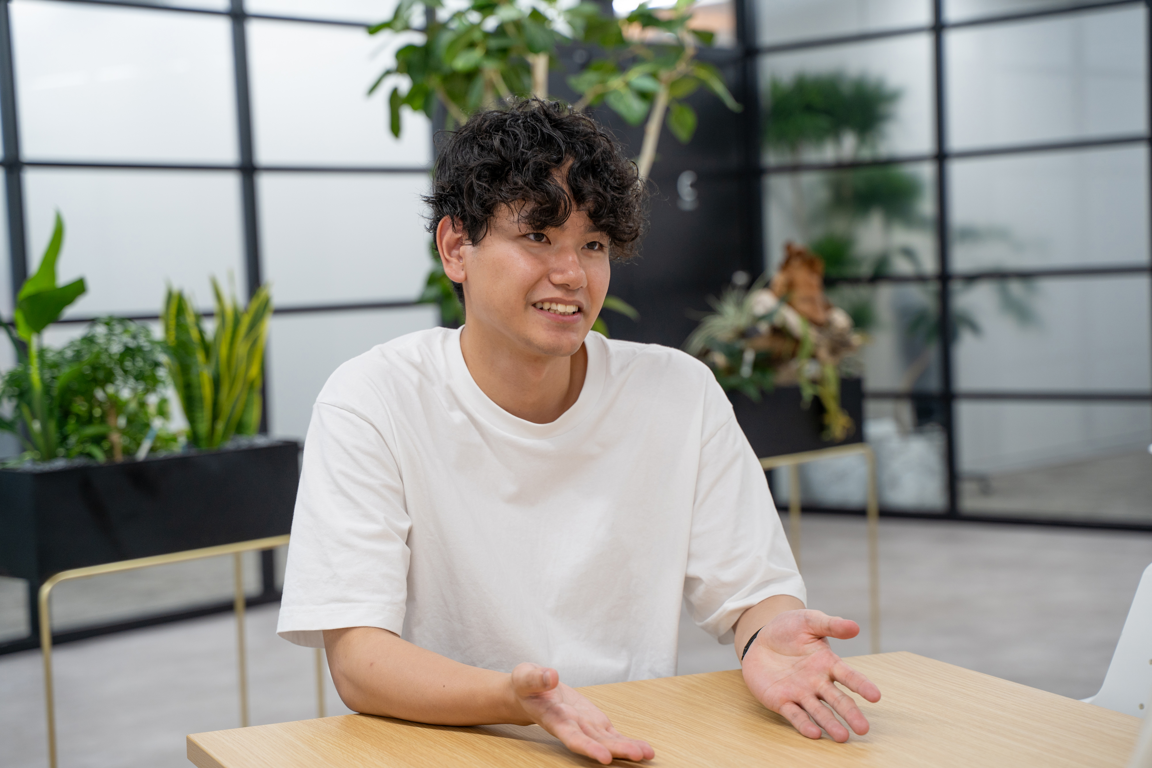 観葉植物のあるオフィスで、身振りを交えながら笑顔で話をする安里さん