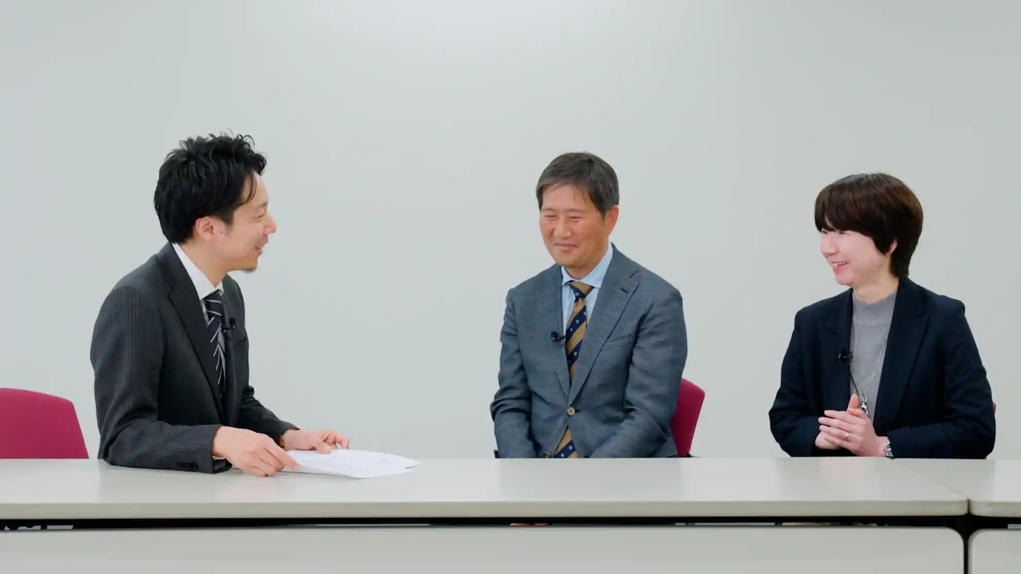 長机を挟んでスーツ姿のビジネスパーソン3名が笑顔で対談している様子。