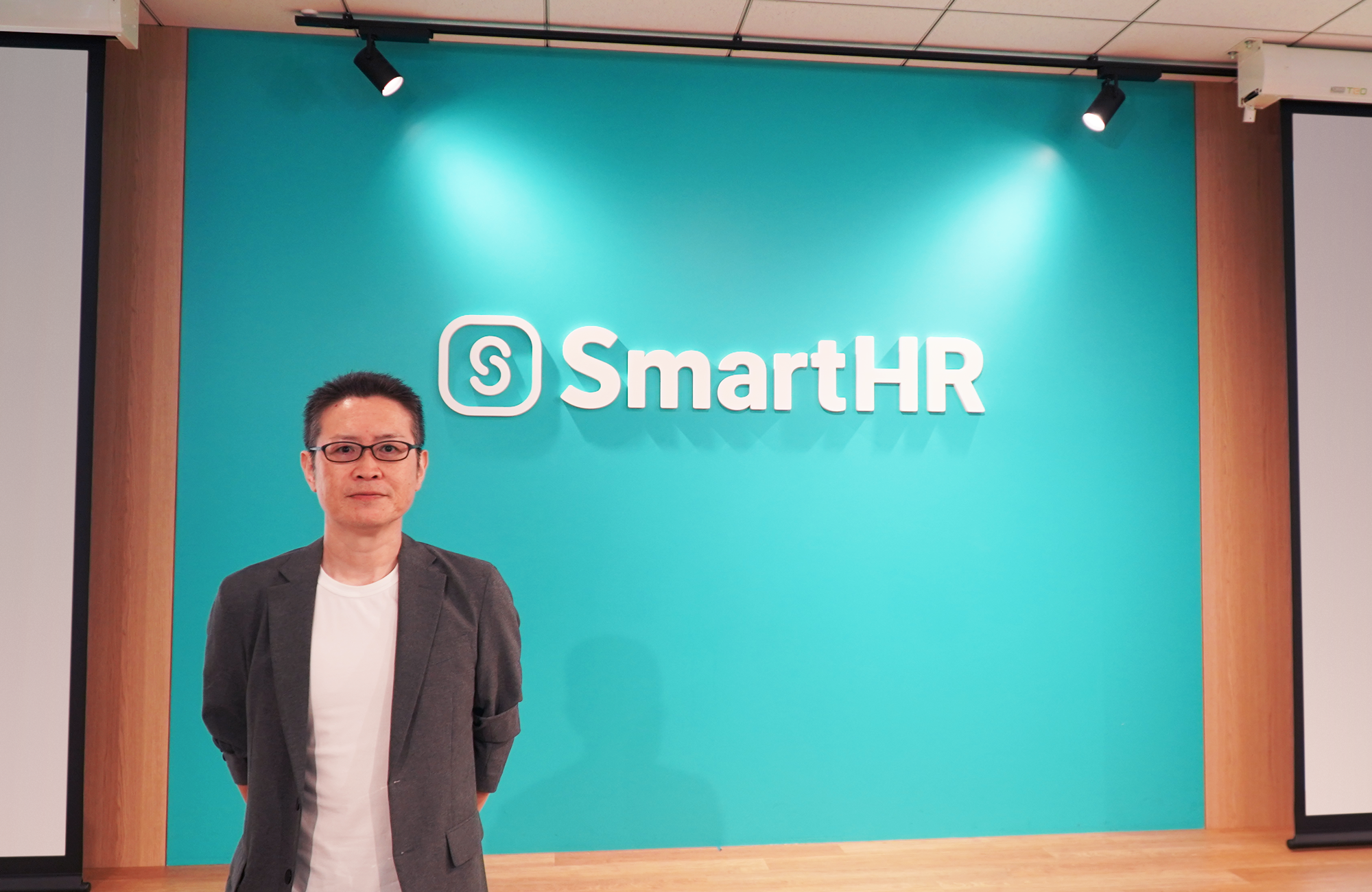 SmartHRのロゴを背景に立っている野口さん