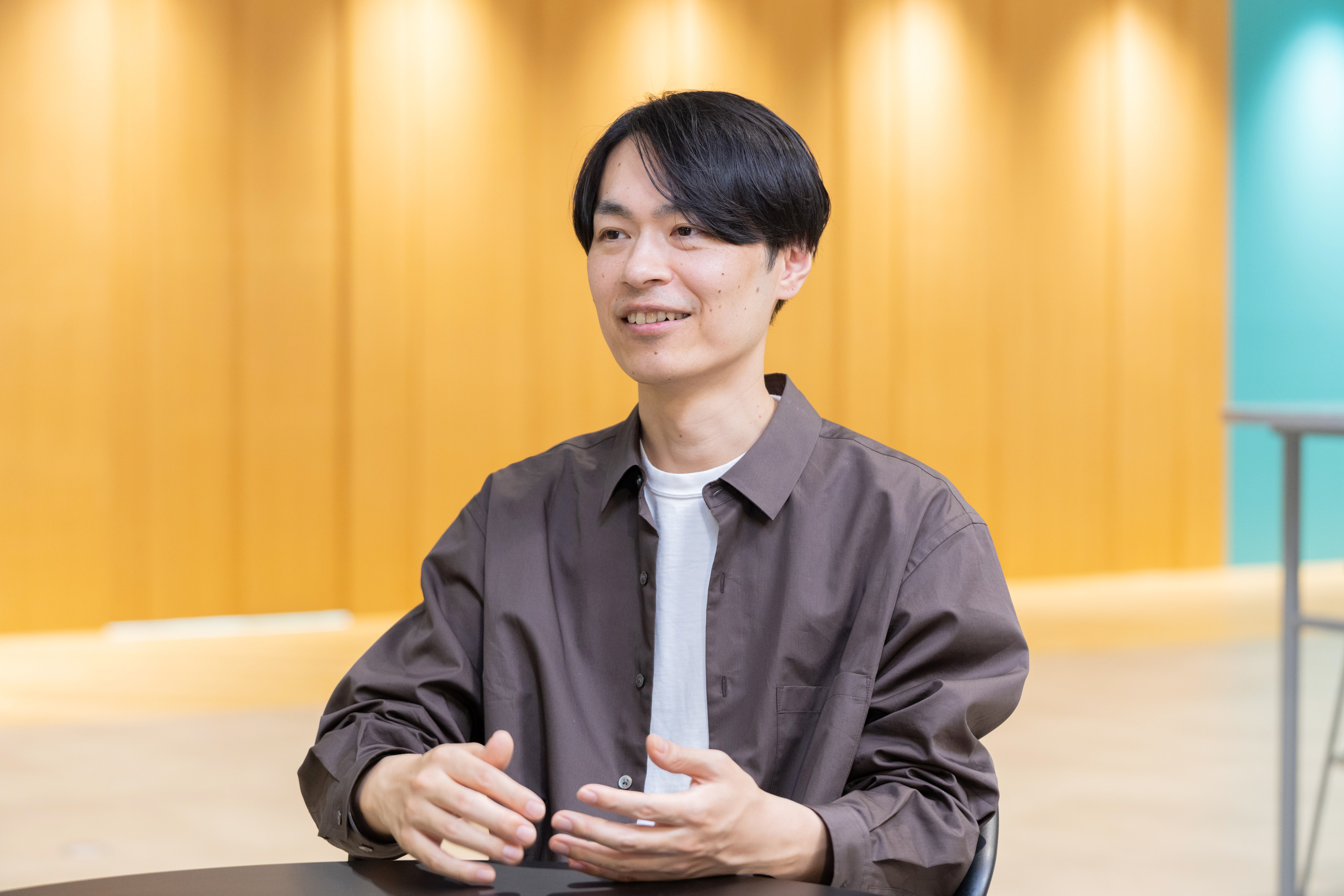 茶色のシャツを着て、身振り手振りを交えながら笑顔で話す男性