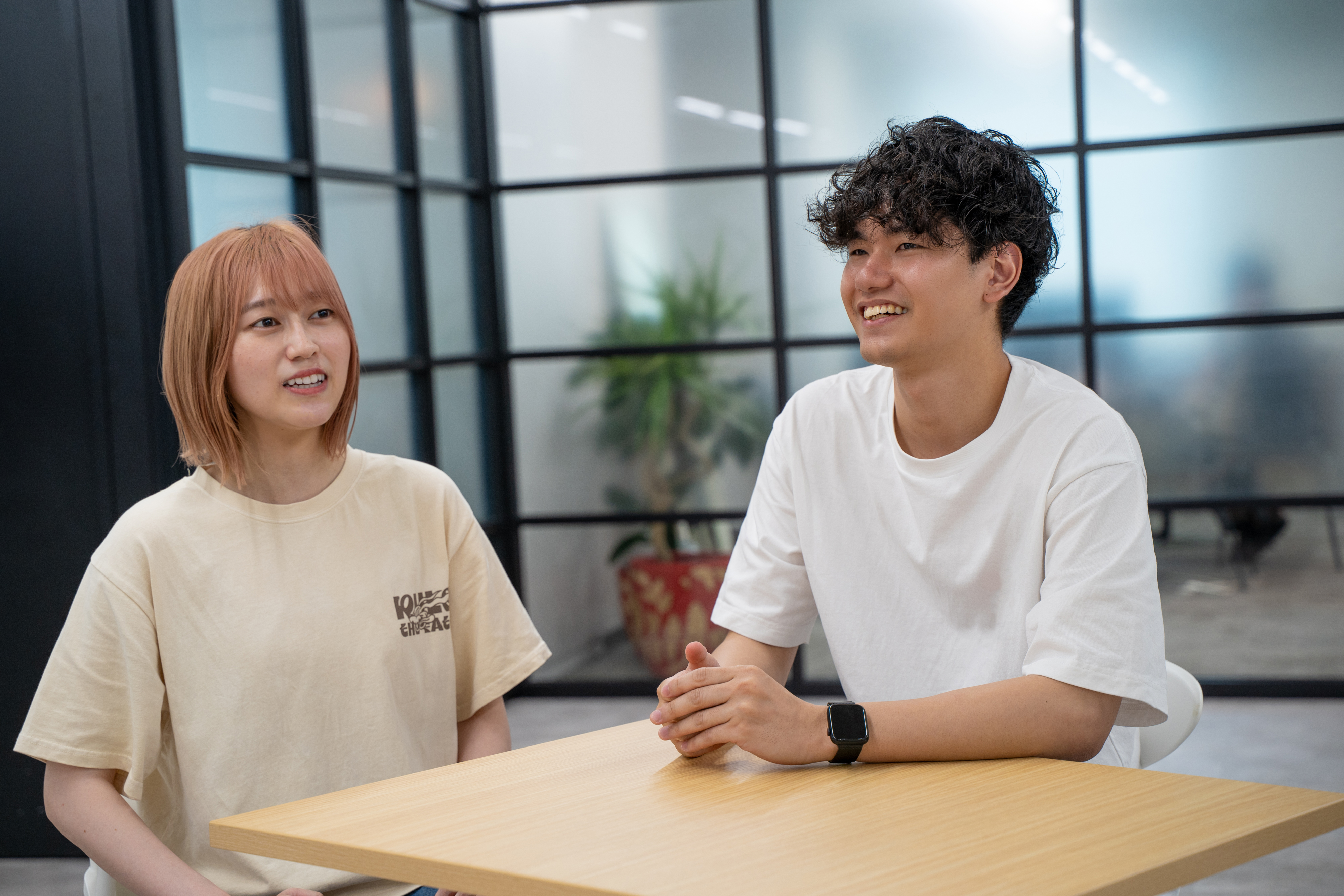 オフィスでテーブルに座り、笑顔で話をする岡田さんと安里さん