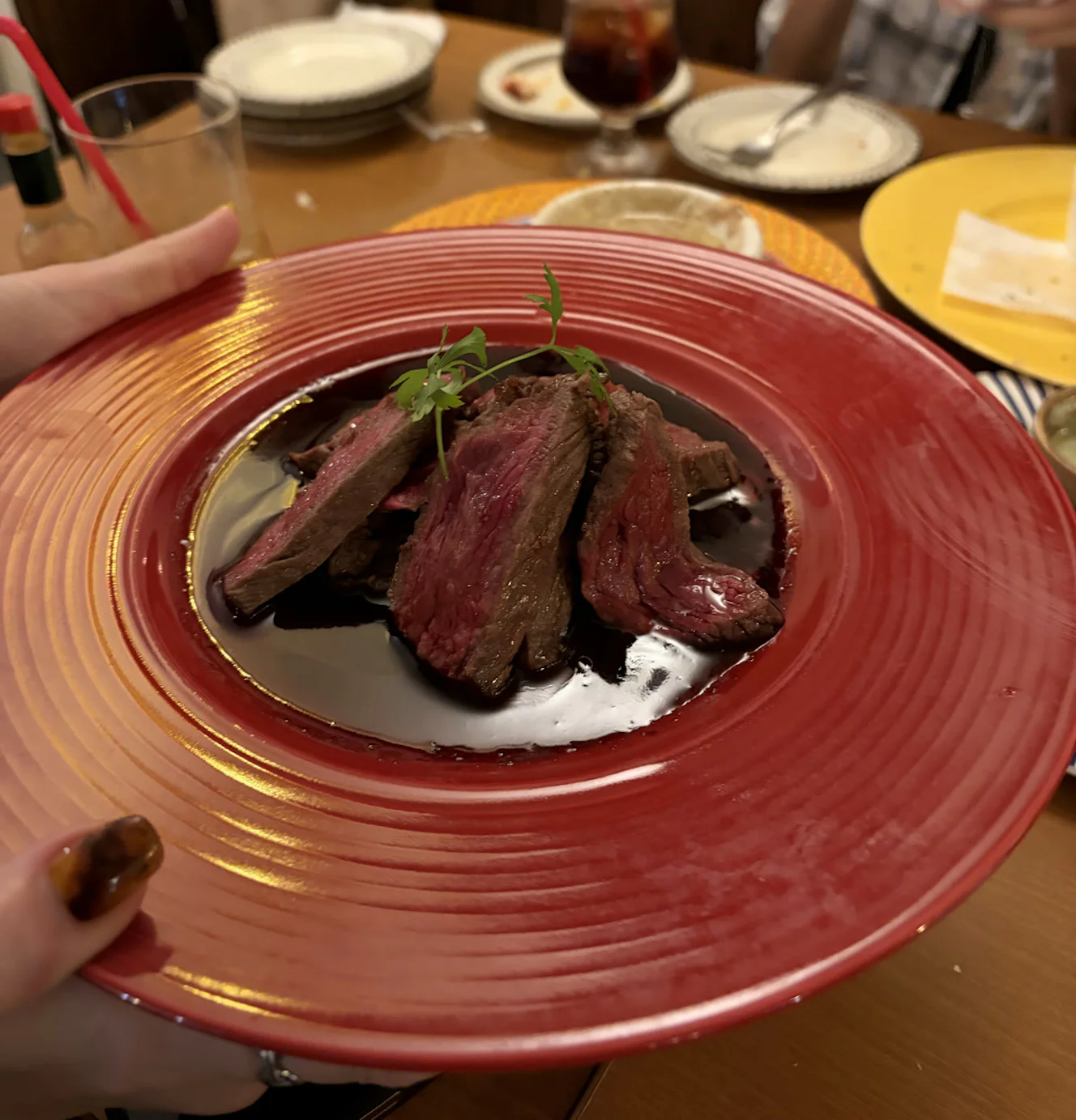 赤い皿に盛られた牛ロースステーキ。赤身のスライスにソースがかかっている