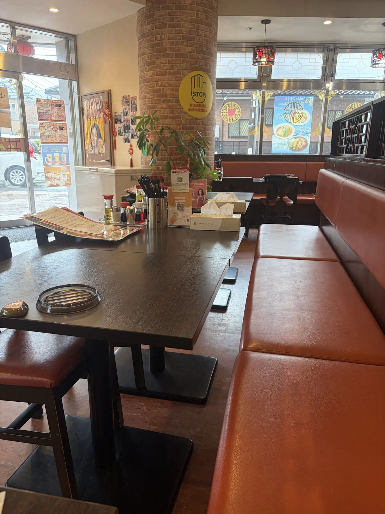 牡丹飯店 北越谷駅店の店内。オレンジのソファ席が壁沿いに並び、レンガ柄の柱と観葉植物がある