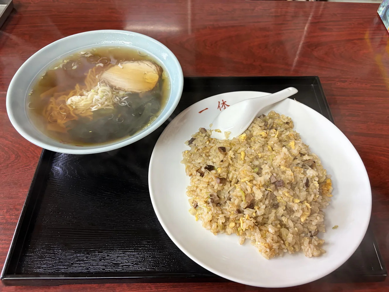 黒いお盆に載って出てきたチャーハン半ラーメンセット。チャーハンの皿と半ラーメンの丼が並んでいる