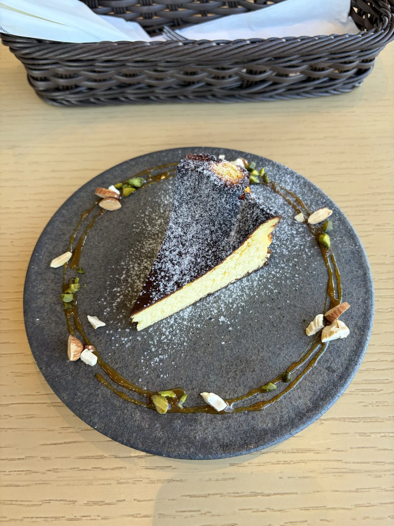 バスクチーズケーキ。粉糖がかかり、皿の周りにソースとナッツが散らしてある