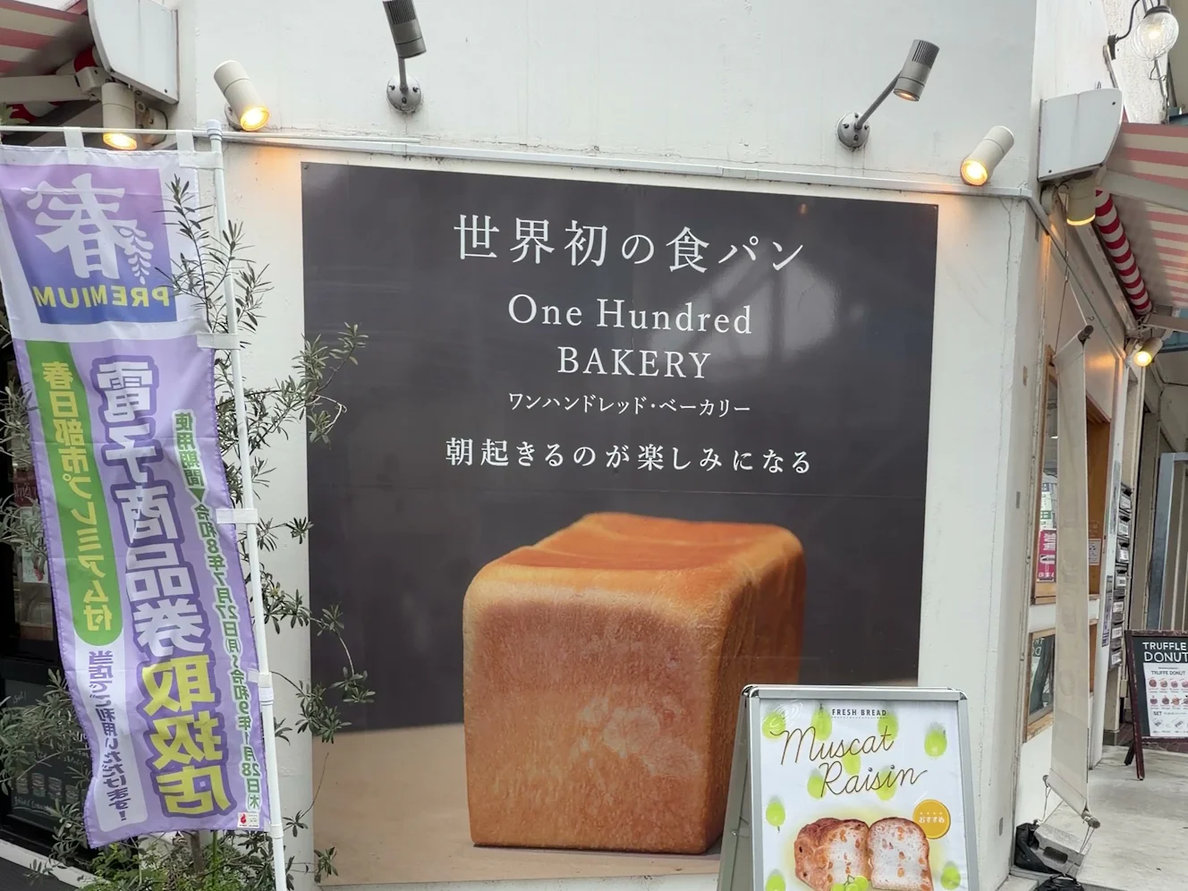 ワンハンドレッドベーカリー春日部店の壁面サイン。「世界初の食パン」「朝起きるのが楽しみになる」の文字と大きな食パンの写真