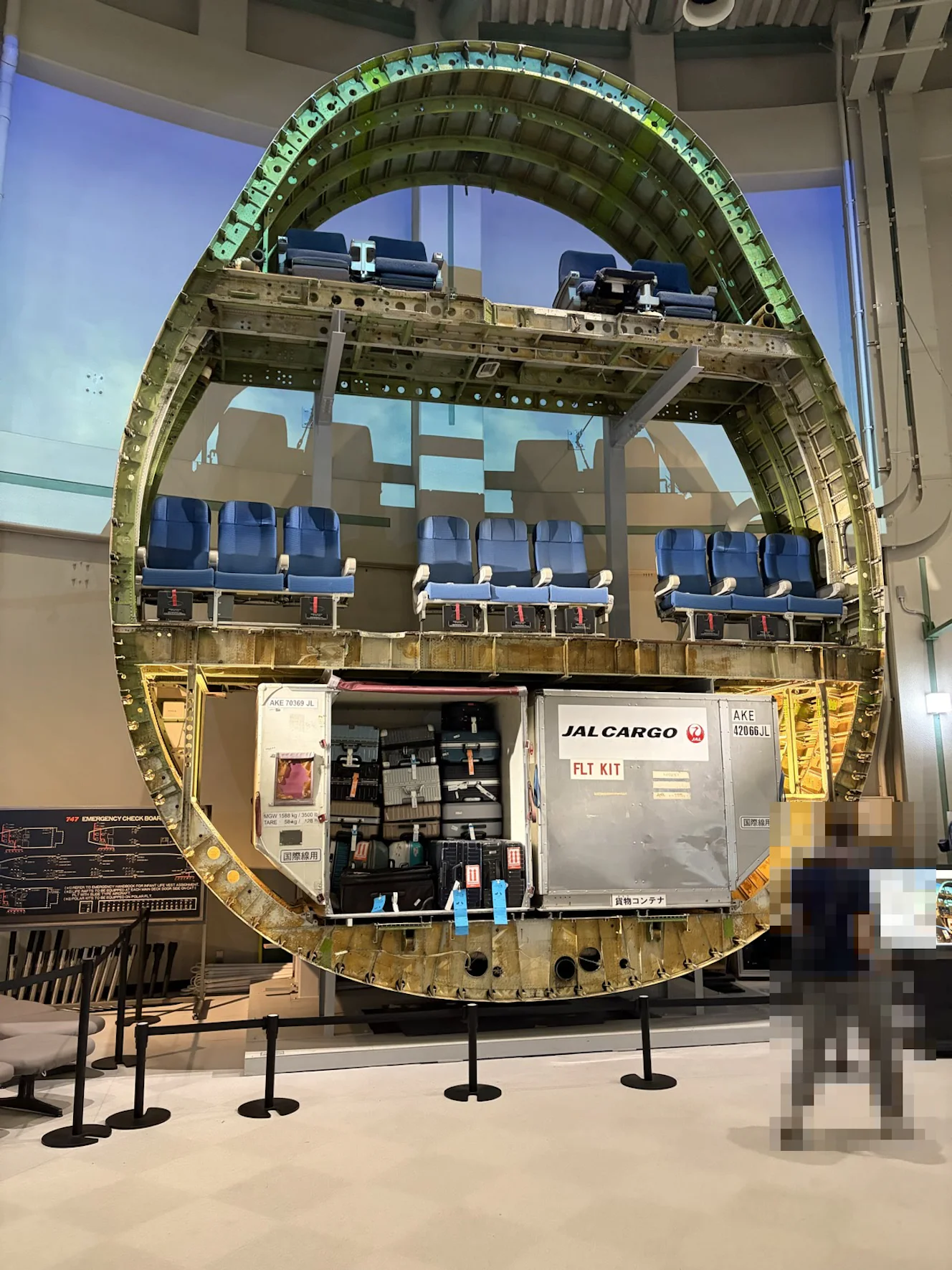ボーイング747の胴体を輪切りにした断面の展示。上から2階席、青い座席の並ぶメインデッキ、床下の貨物コンテナとスーツケース