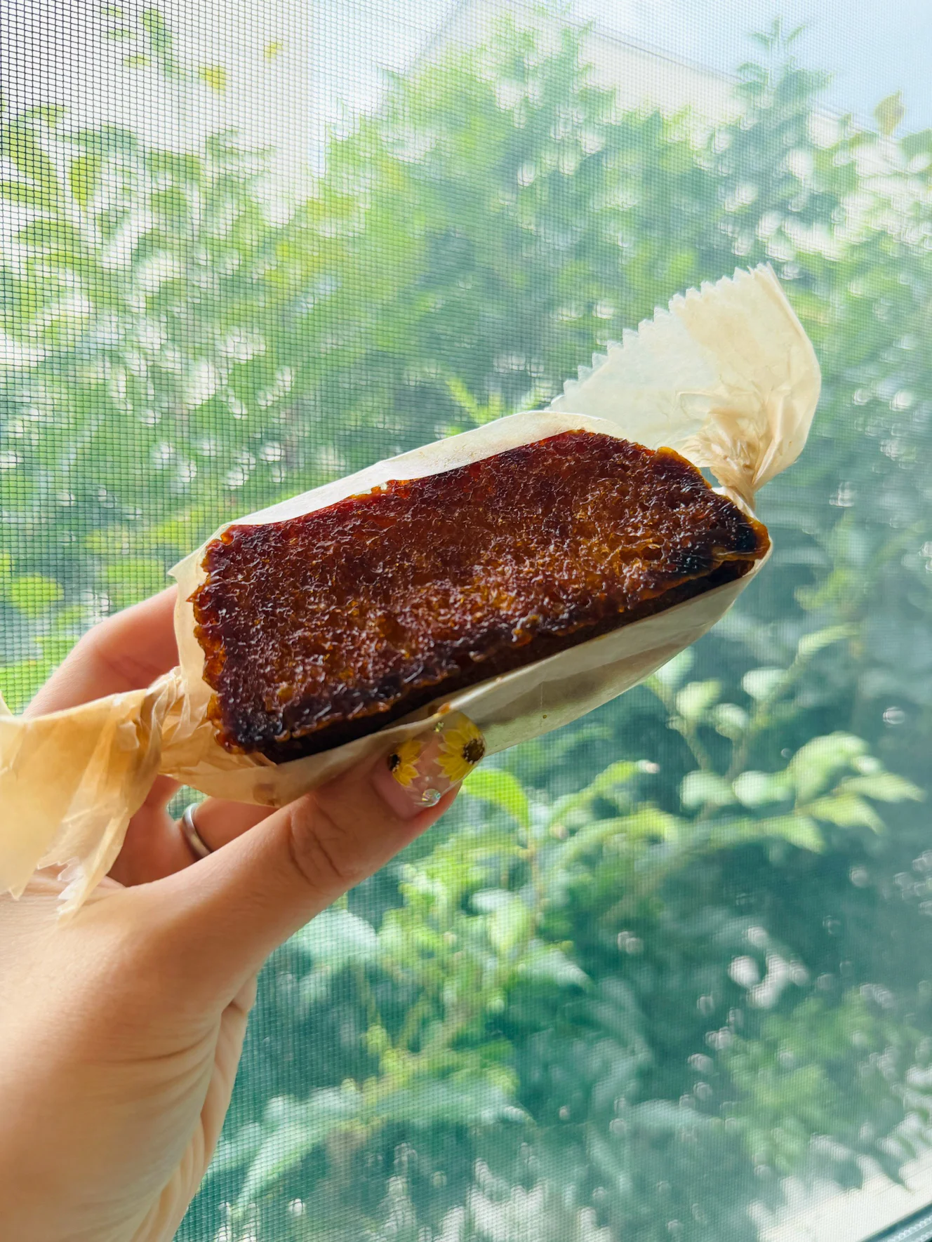 ハニートースト。上面全体が濃い茶色にキャラメリゼされ、紙に包まれて手に持たれている