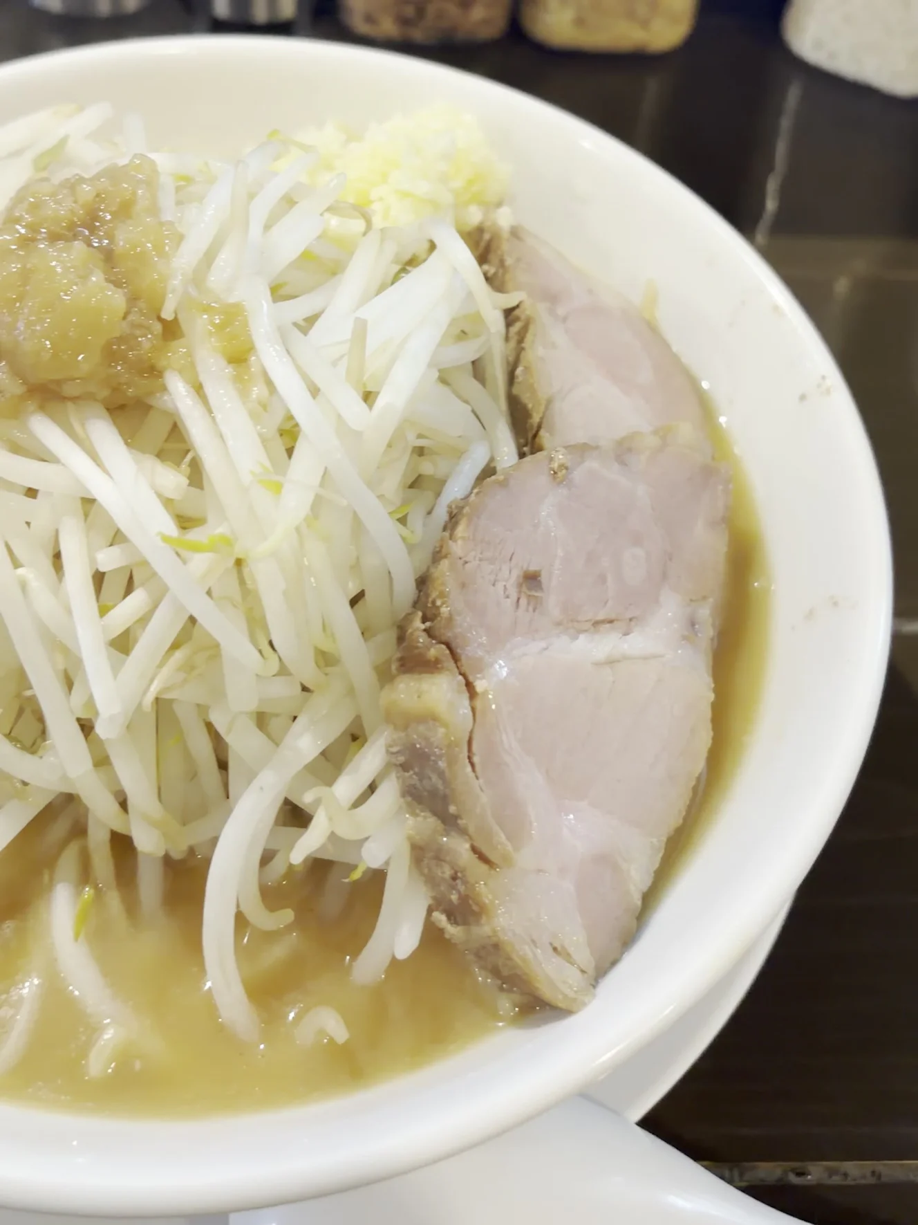 着丼したラーメン野菜。もやしの山の上ににんにくとあぶらが乗り、右手に厚切りのチャーシューが見える