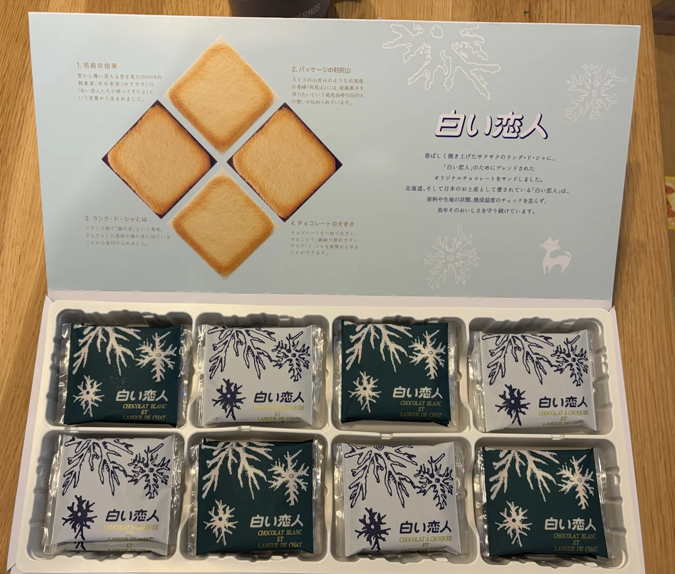 箱を開けた白い恋人。濃い緑と白の個包装が市松に並び、内蓋に解説文が印刷されている
