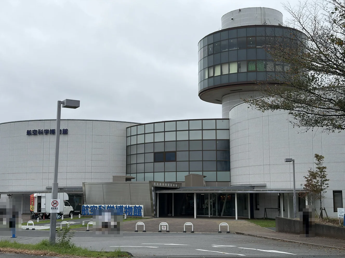 航空科学博物館の外観。曇り空の下、展望塔のある建物の前に、青い「航空科学博物館」の立体文字が立っている