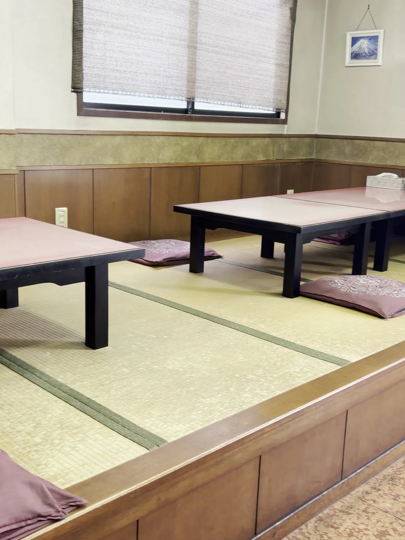 一休の畳の小上がり。ピンクの天板の座卓とえんじの座布団が並び、窓にはすだれが下がっている