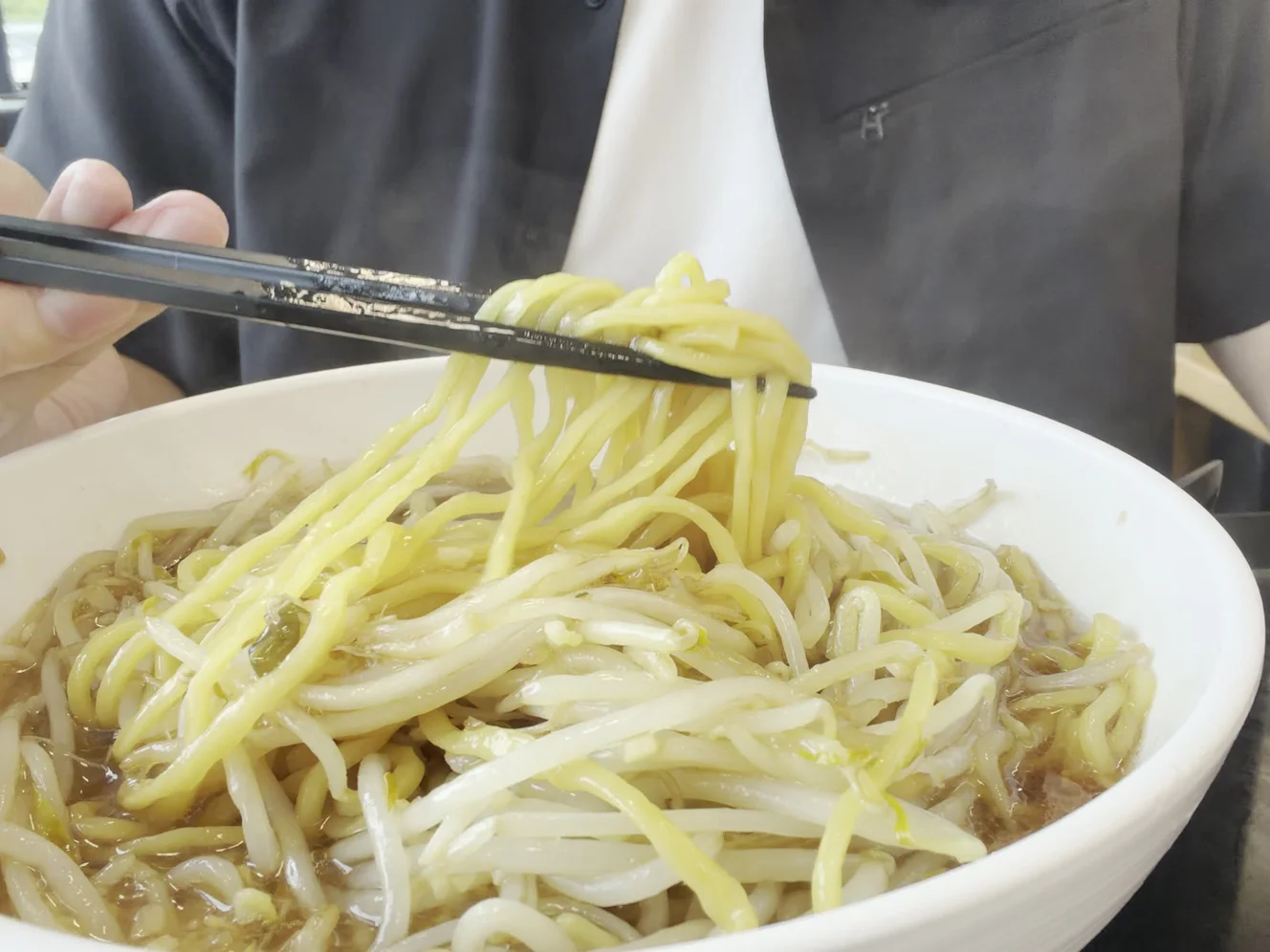 箸で持ち上げた酒々郎ラーメンの麺。丼の中で黄色い麺ともやしが混ざっている