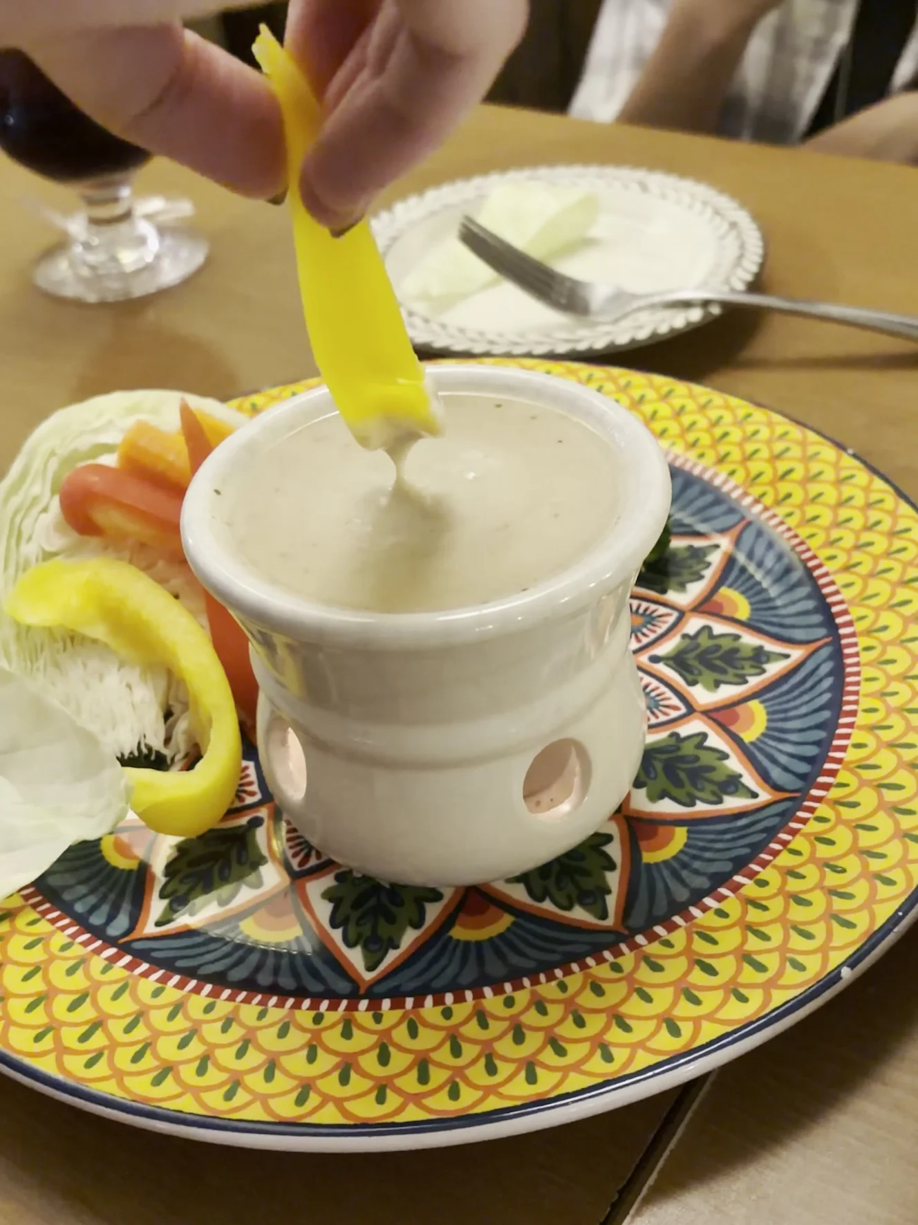 バーニャカウダ。黄色い皿の野菜と、ポットで温めたソースにパプリカを付けているところ