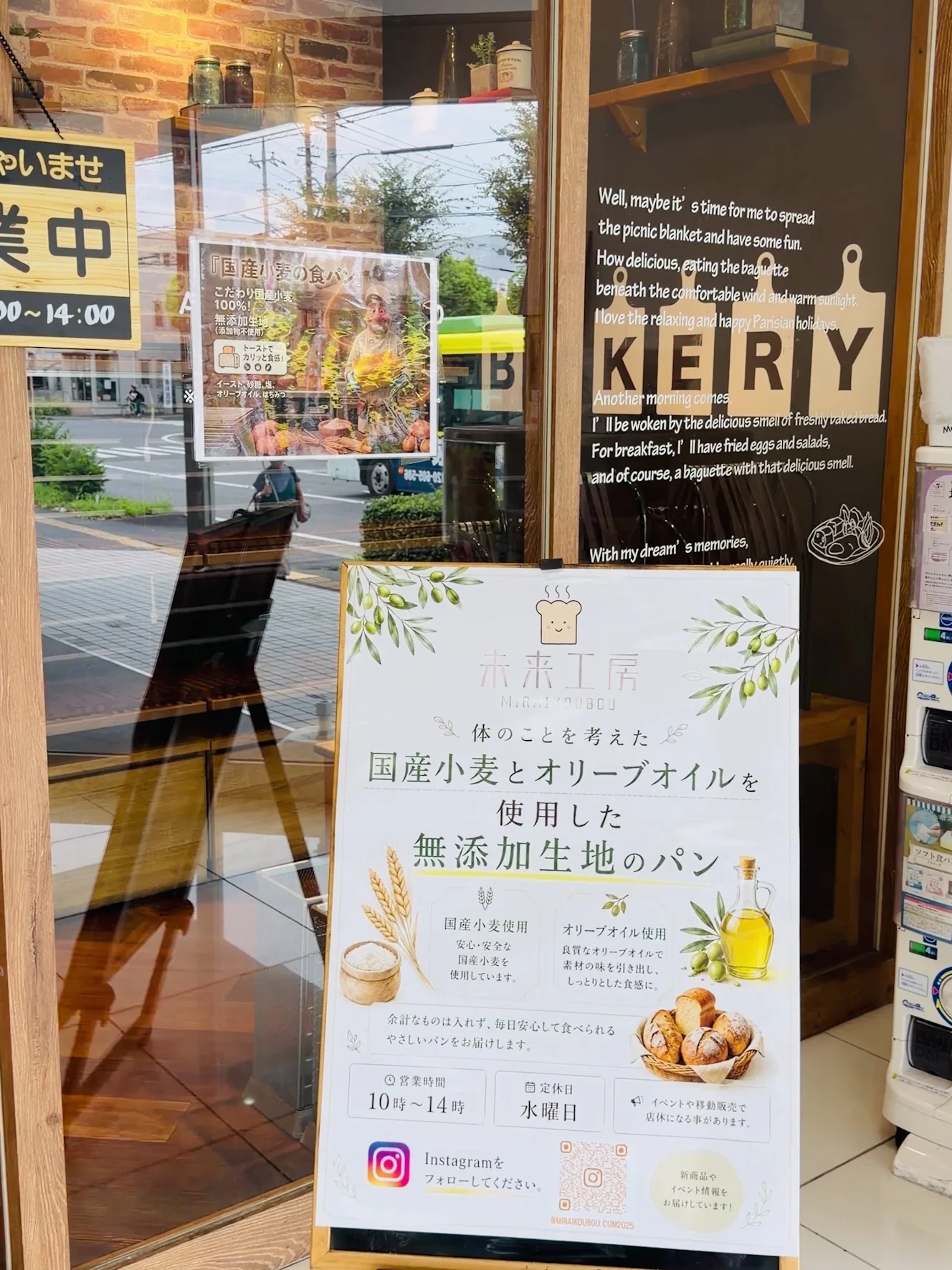 未来工房の店頭に立つ案内看板。国産小麦とオリーブオイルを使用した無添加生地のパン、営業時間10時から14時、定休日は水曜日と書かれている