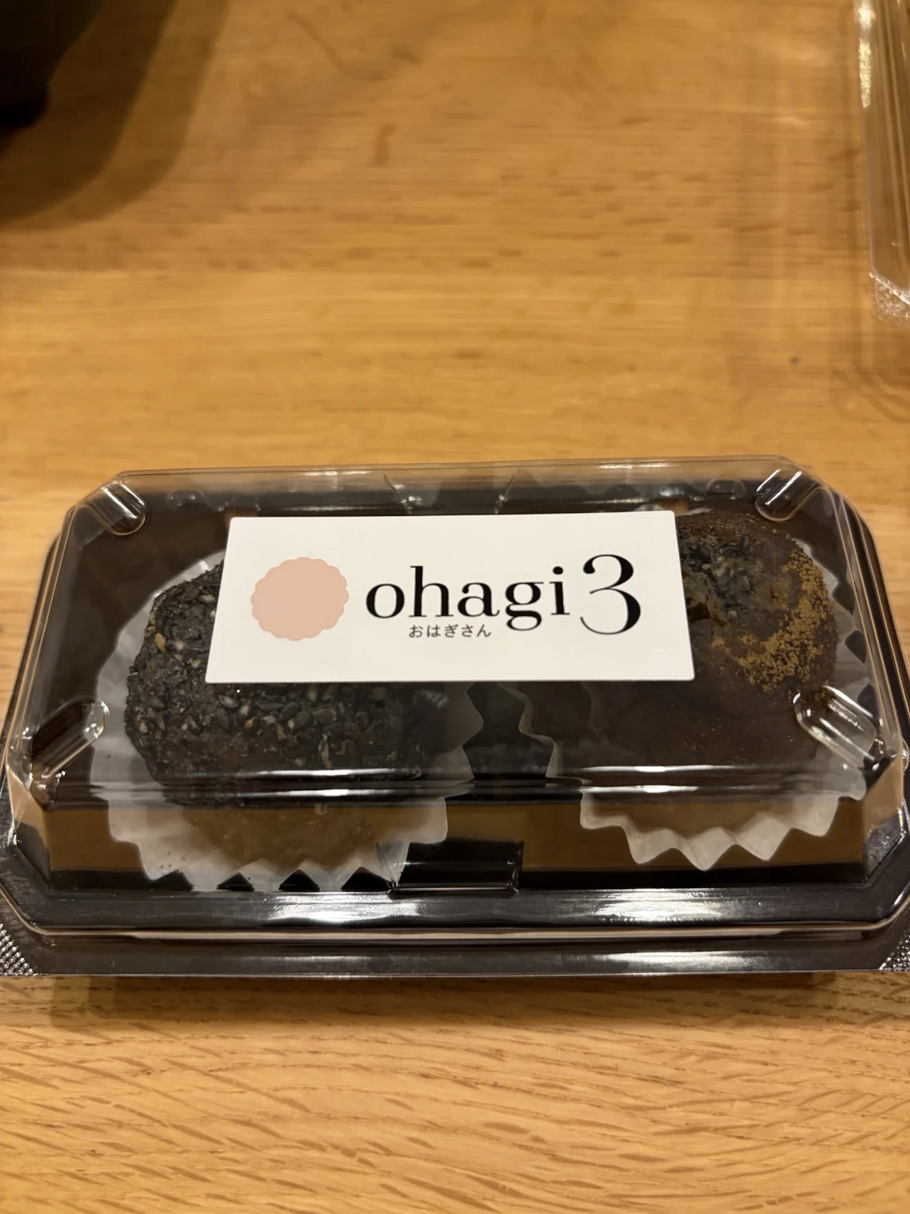 ohagi3のロゴ帯が掛かった2個入りパック。フタ越しに黒ゴマとほうじ茶のおはぎが見える