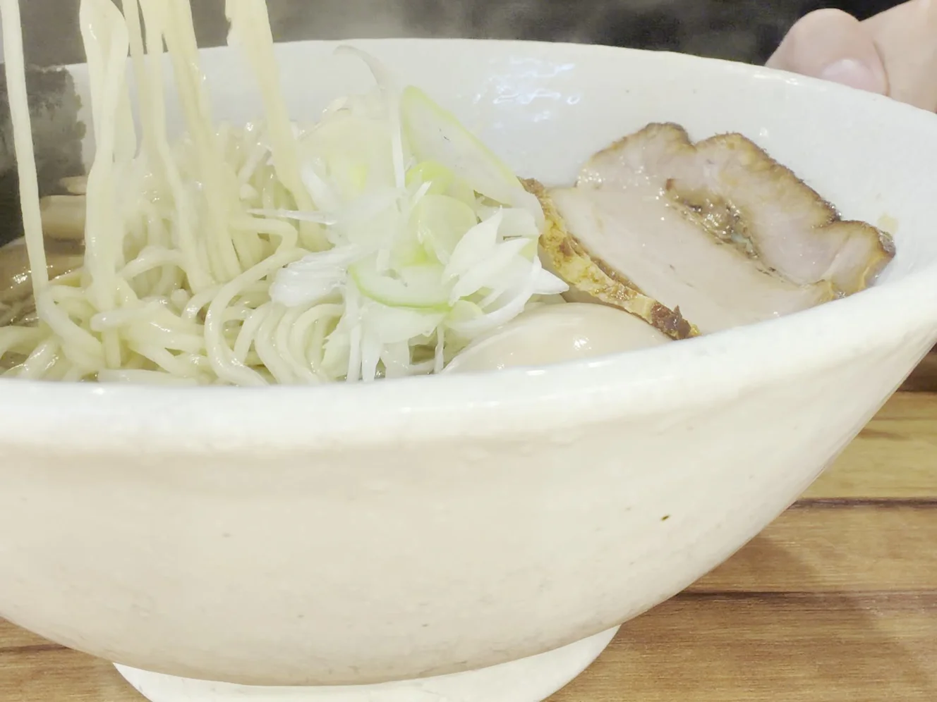 箸で持ち上げた細いストレート麺。丼の中にさらしネギ、チャーシュー、味玉が見える