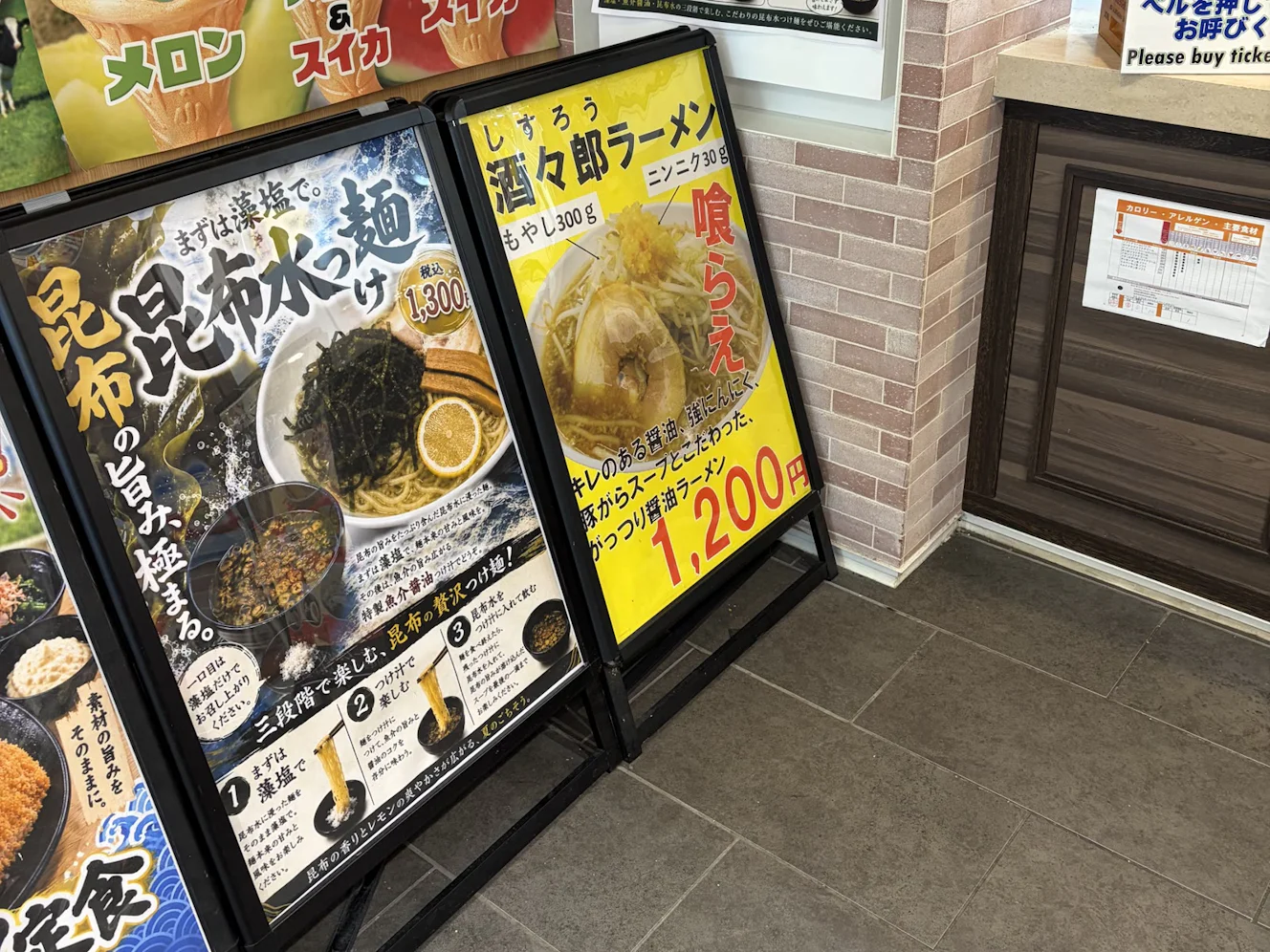 酒々井PA（下り）のフードコート店頭にある酒々郎ラーメンの立て看板。黄色地に「もやし300g」「ニンニク30g」「1,200円」と書かれている