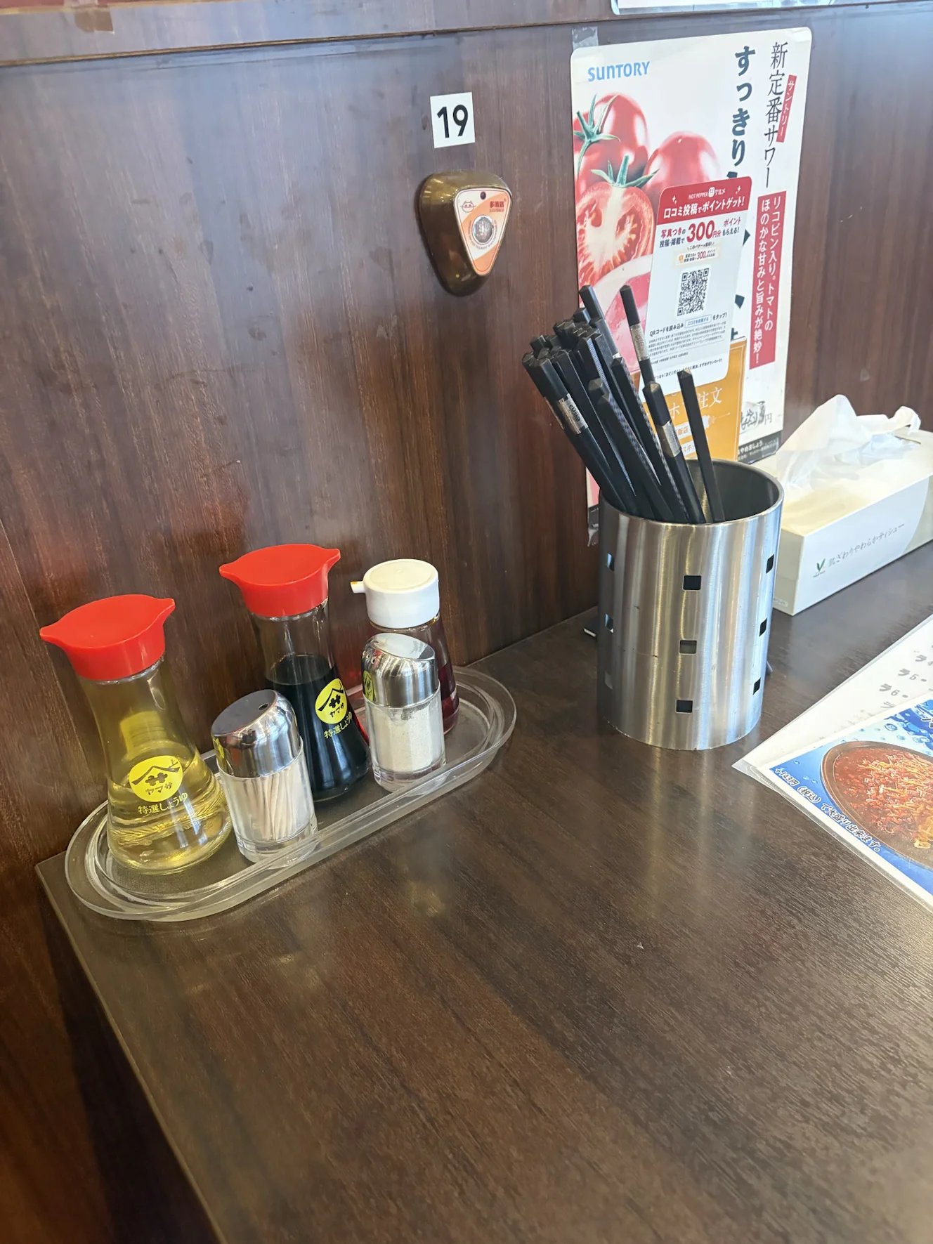 卓上の調味料。酢・しょうゆ・ラー油・胡椒と箸立てが置かれ、壁にテーブル番号と呼び出しボタンがある