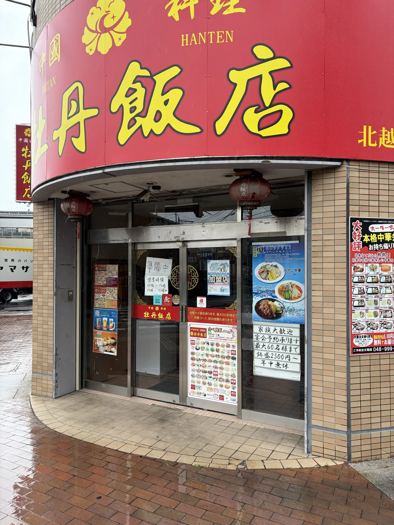 牡丹飯店 北越谷駅店の外観。赤い看板に黄色い文字で店名があり、入口の上に赤い提灯が2つ下がっている