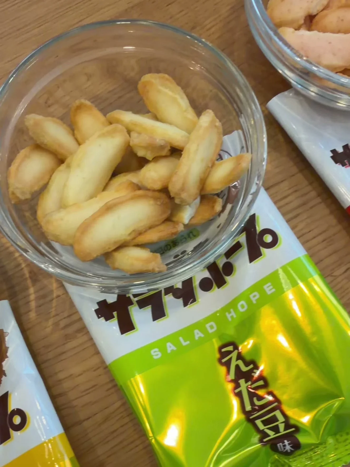 ガラスの器に出したえだ豆味のあられ。緑のえだ豆味の小袋の上に器が乗っている