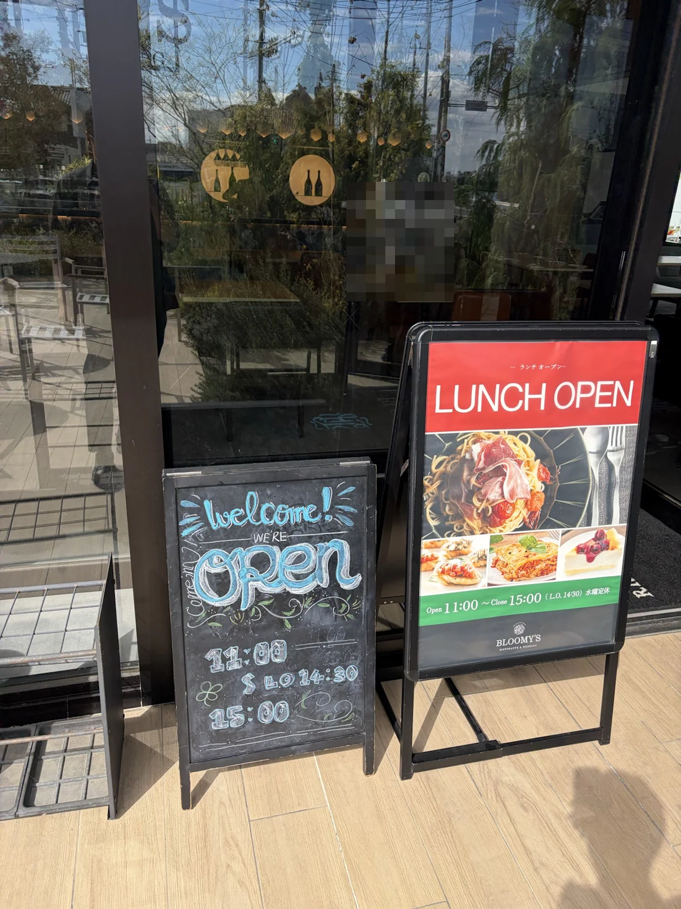 店の入口。「Welcome! WE'RE open」と書かれた黒板と、赤い「LUNCH OPEN」の看板が並んでいる