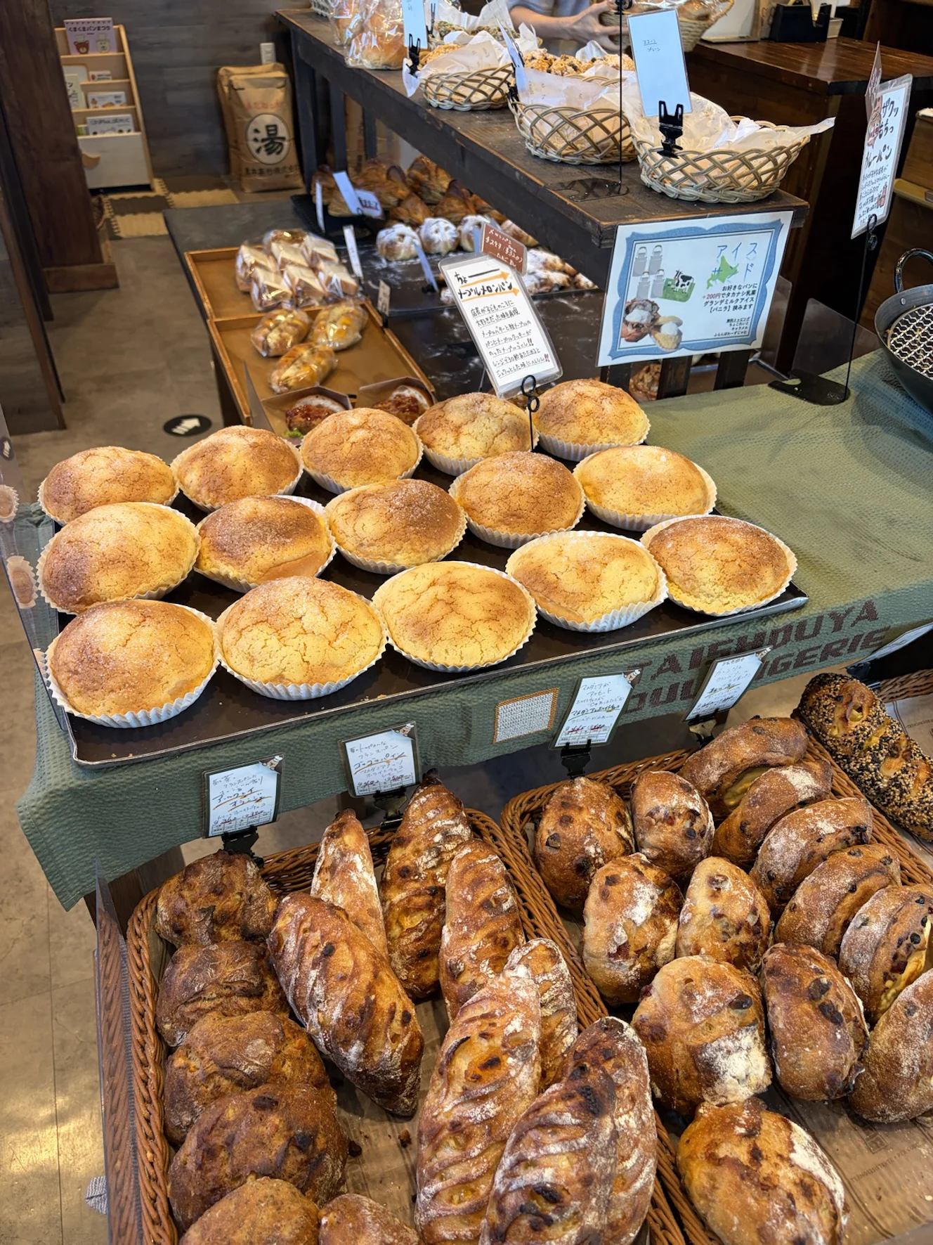 店内の陳列。手前にグラニュー糖をまぶしたマフィン型の焼き菓子、奥にはハード系のパンがバスケットいっぱいに並ぶ