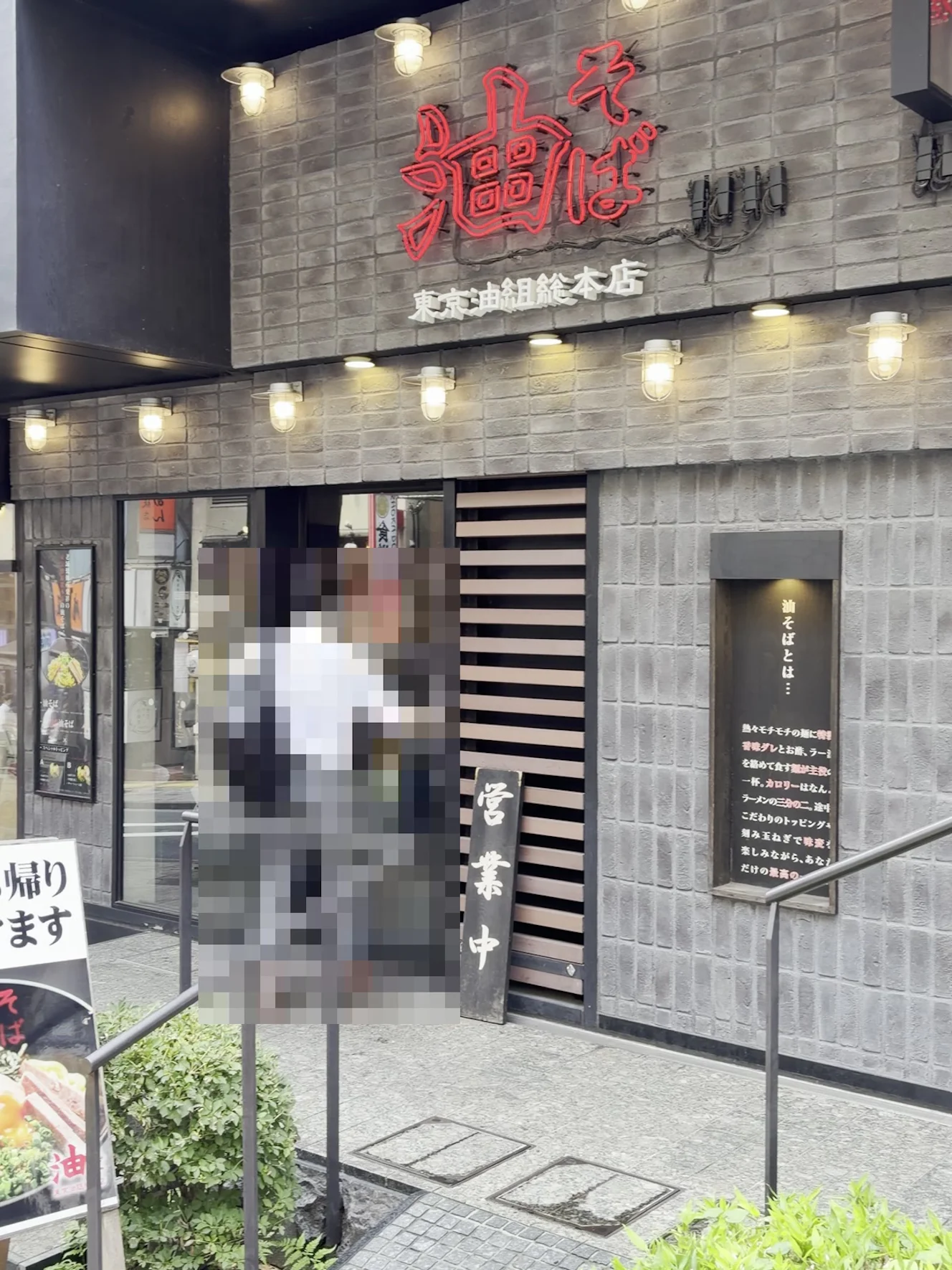東京油組総本店 神楽坂組の外観。グレーのレンガ壁に赤いネオンの「油そば」の看板と、入口の営業中の木札
