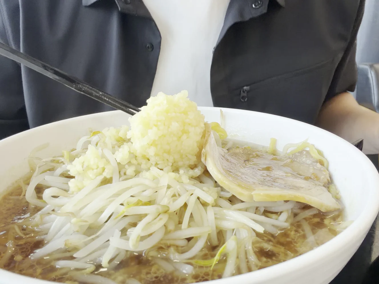 酒々郎ラーメンの寄り。もやしの上に刻みにんにくの山があり、横に大判のチャーシューが1枚載っている