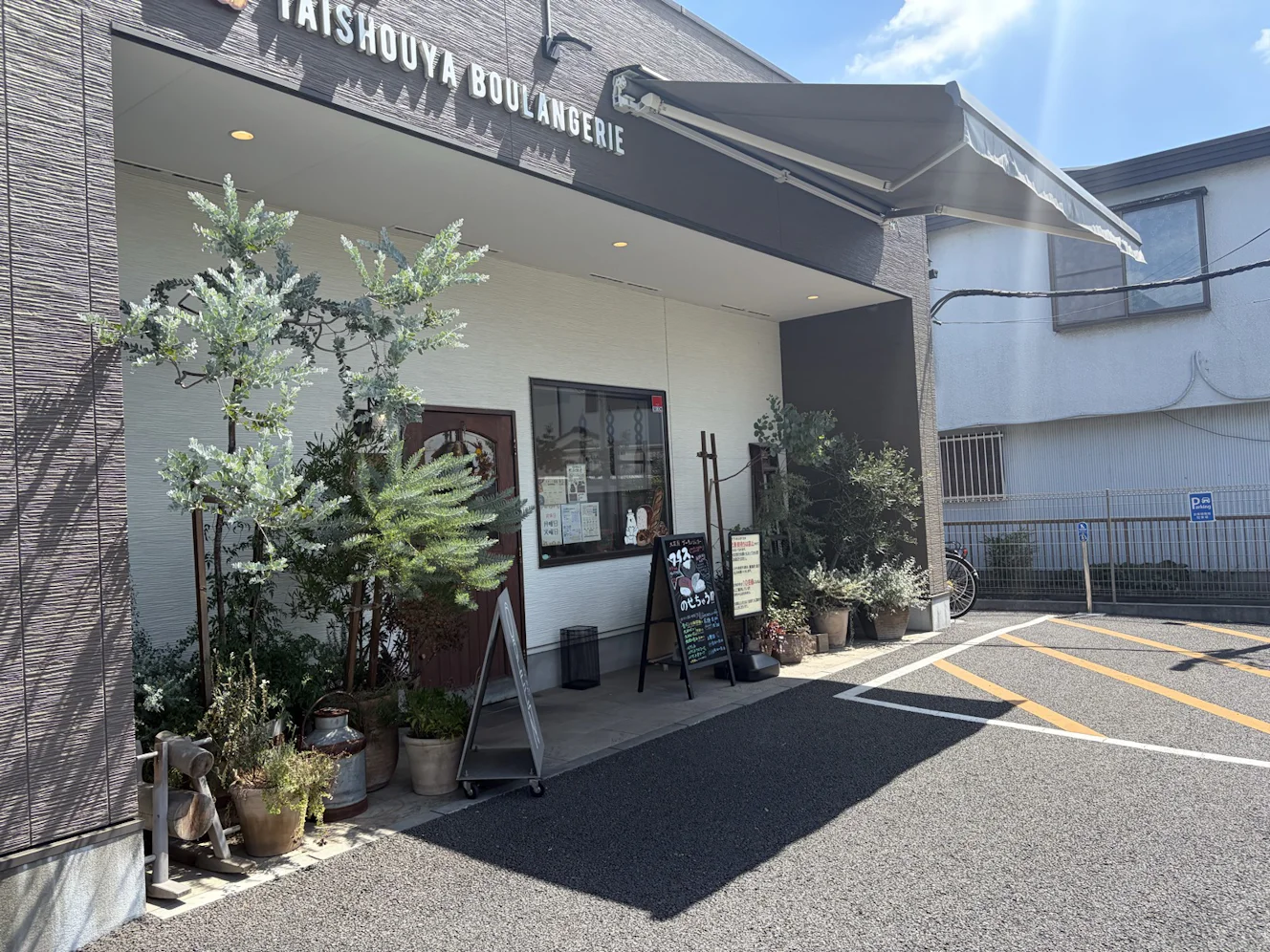 大正屋Boulangerieの外観。木目調と白壁の建物に黒いオーニングがかかり、TAISHOUYA BOULANGERIEのロゴ看板が目を引く