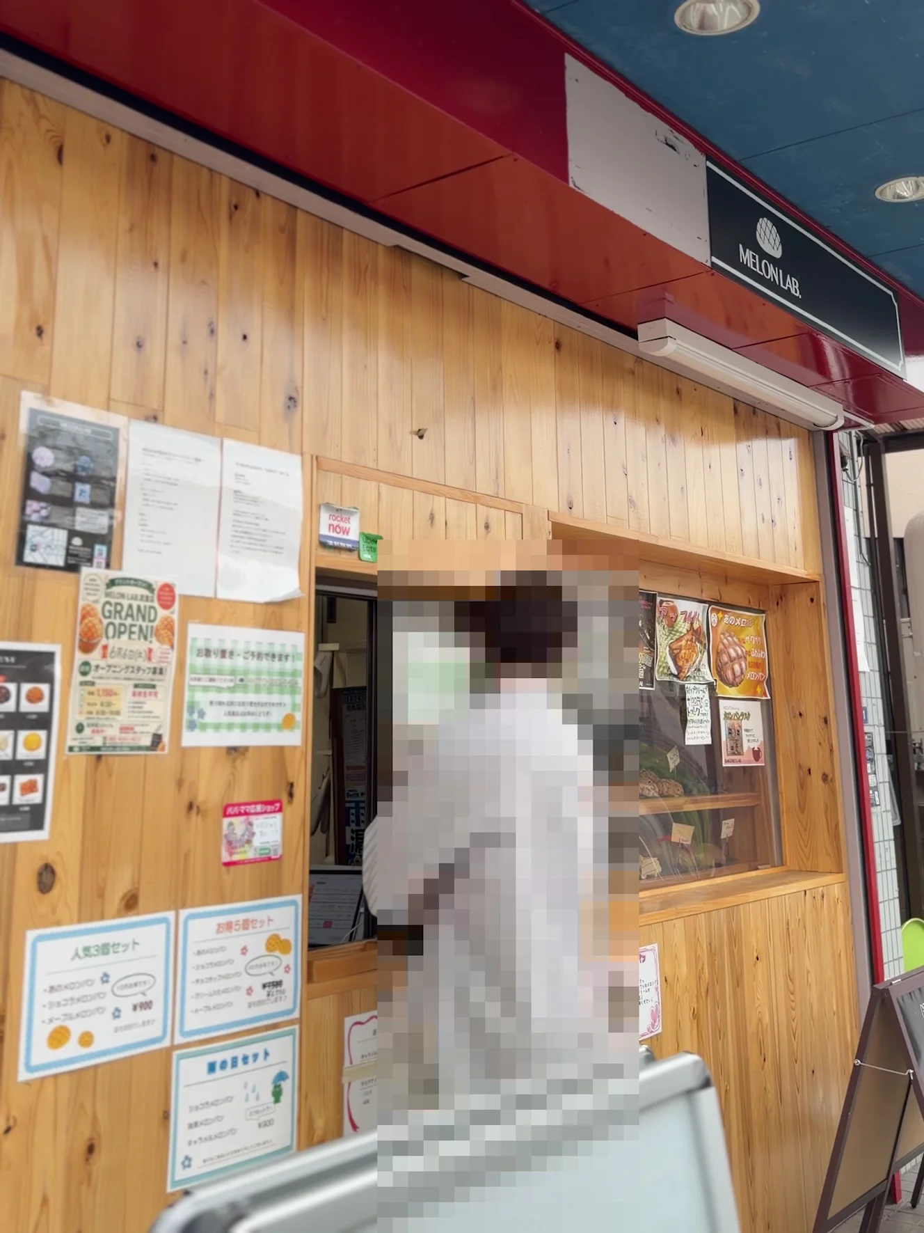 メロンラボ越谷店の店頭。赤い庇の下にMELON LAB.の看板、木目の壁に貼り紙とメニュー
