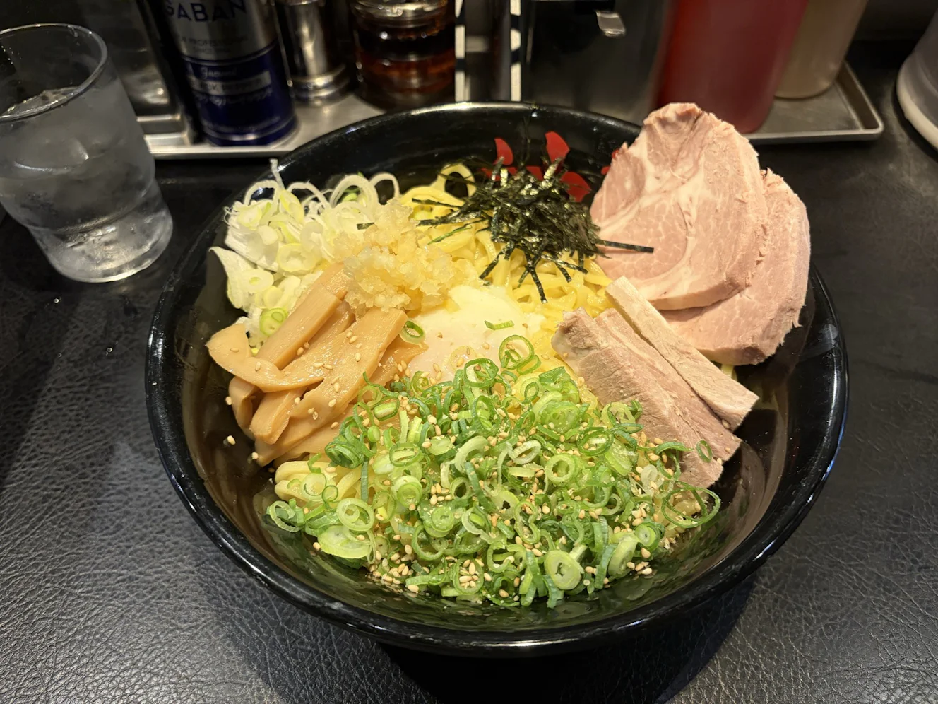 着丼直後の油そばW盛り。太い麺の上にチャーシュー、刻みのり、白ねぎ、青ねぎとゴマ、メンマ、半熟卵、つぶし生にんにく